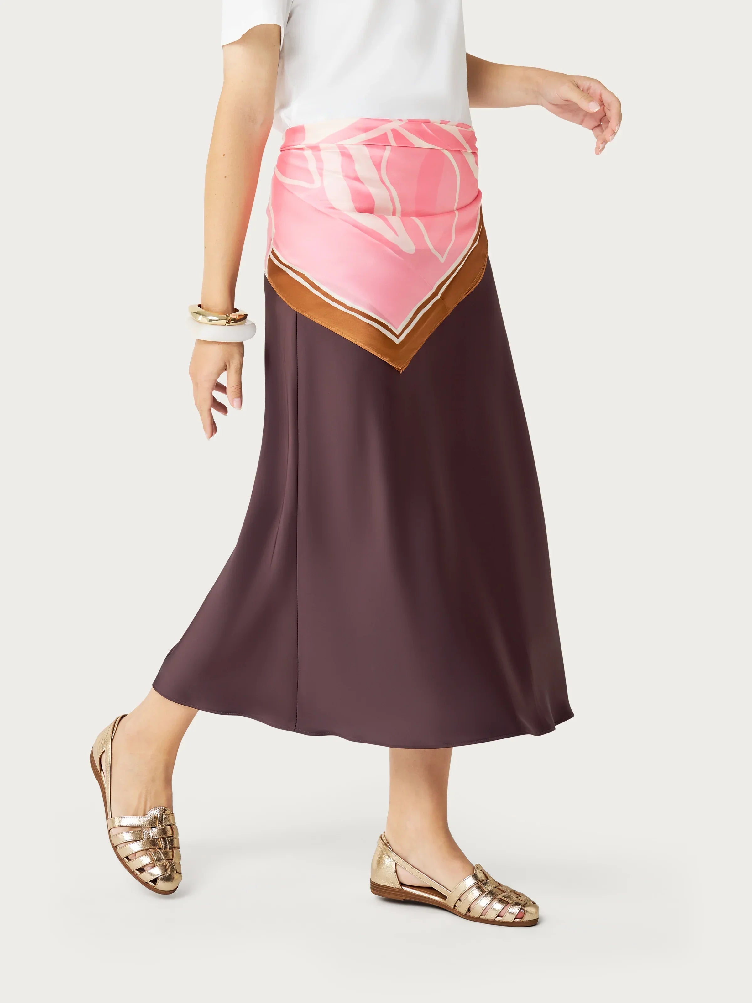 Donna con gonna lunga marrone, foulard rosa in vita e sandali dorati, stile elegante