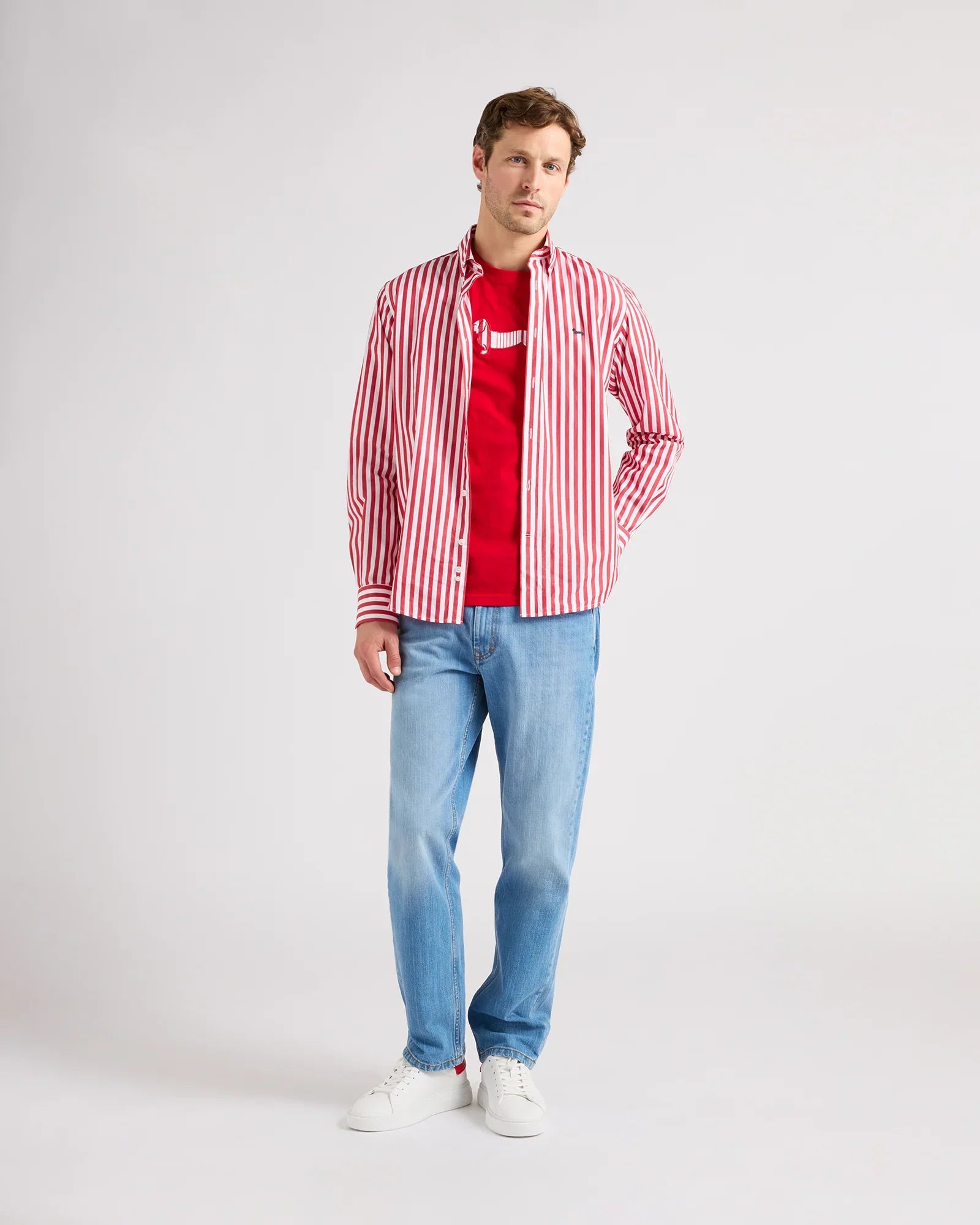 Modello uomo con camicia a righe rosse e bianche, t-shirt rossa, jeans chiari e sneakers bianche