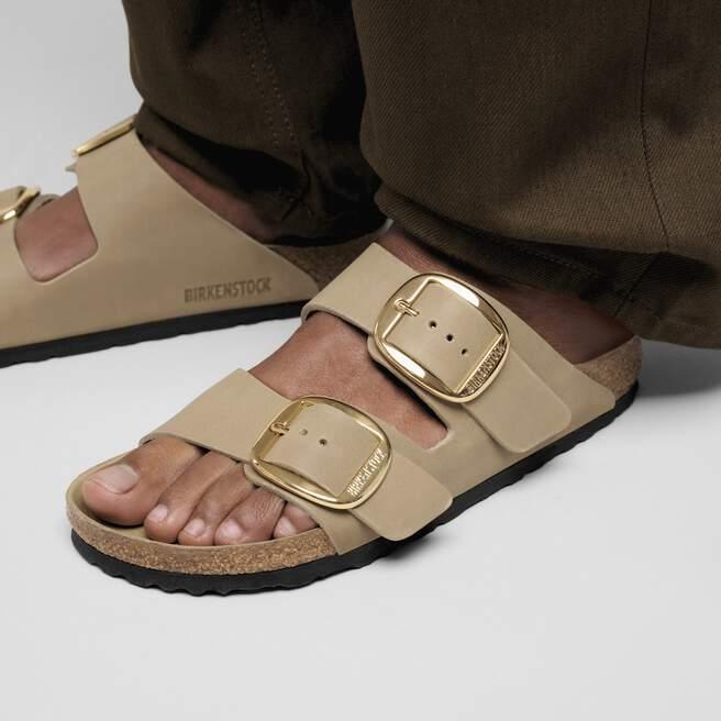 Sandali beige Birkenstock con cinturini e fibbie dorate, dettaglio su piede maschile.