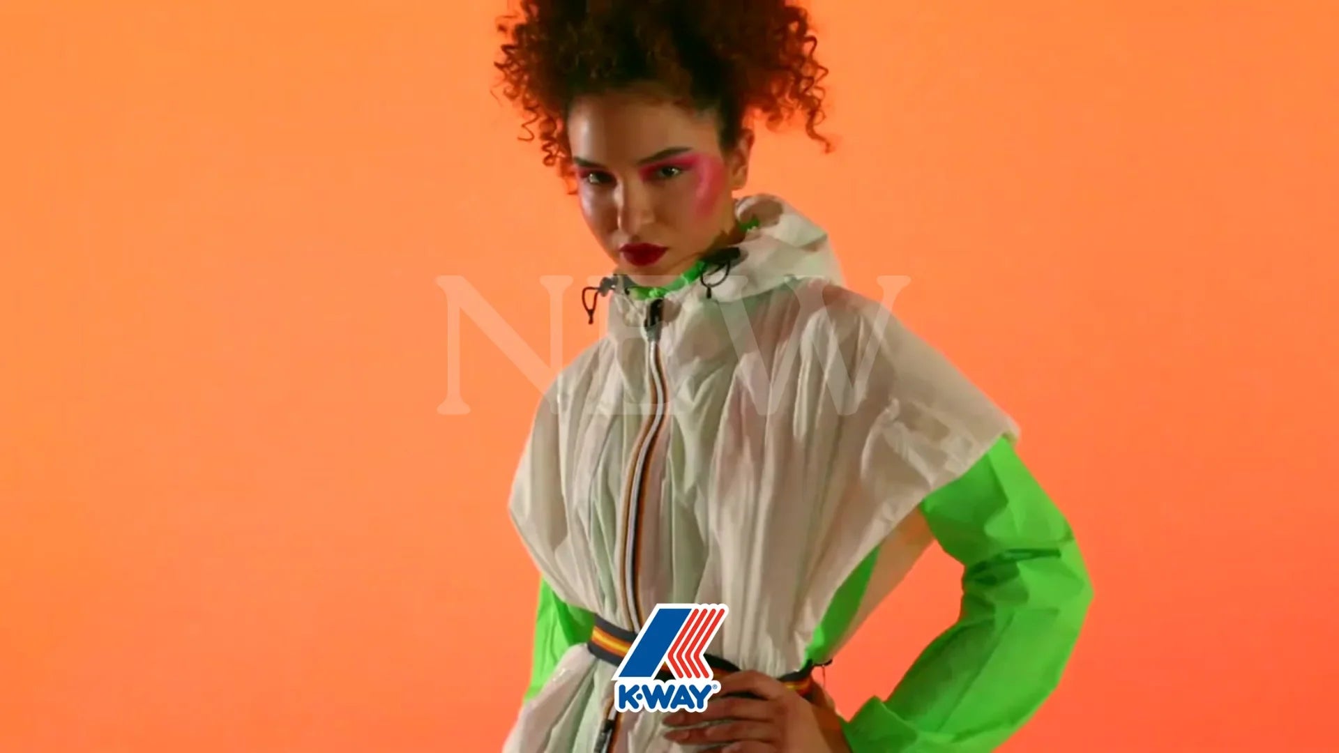 Modella con giacca K-Way bianca e verde fluo su sfondo arancione, look sportivo moderno.