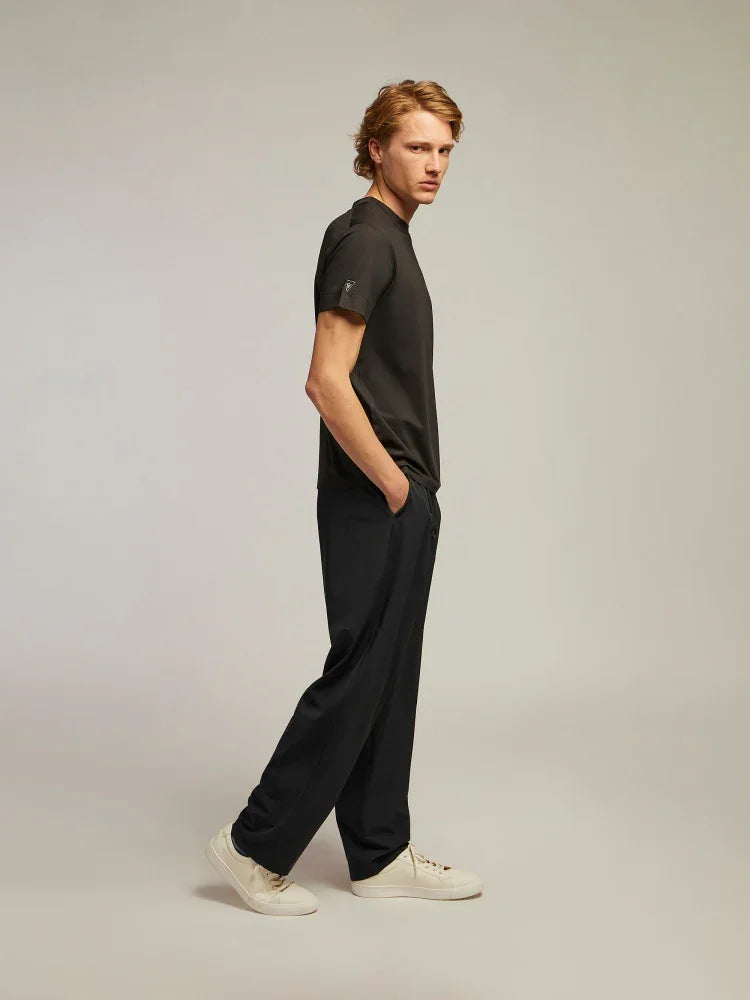 Modello uomo con t-shirt nera, pantaloni neri larghi e sneakers bianche su sfondo neutro