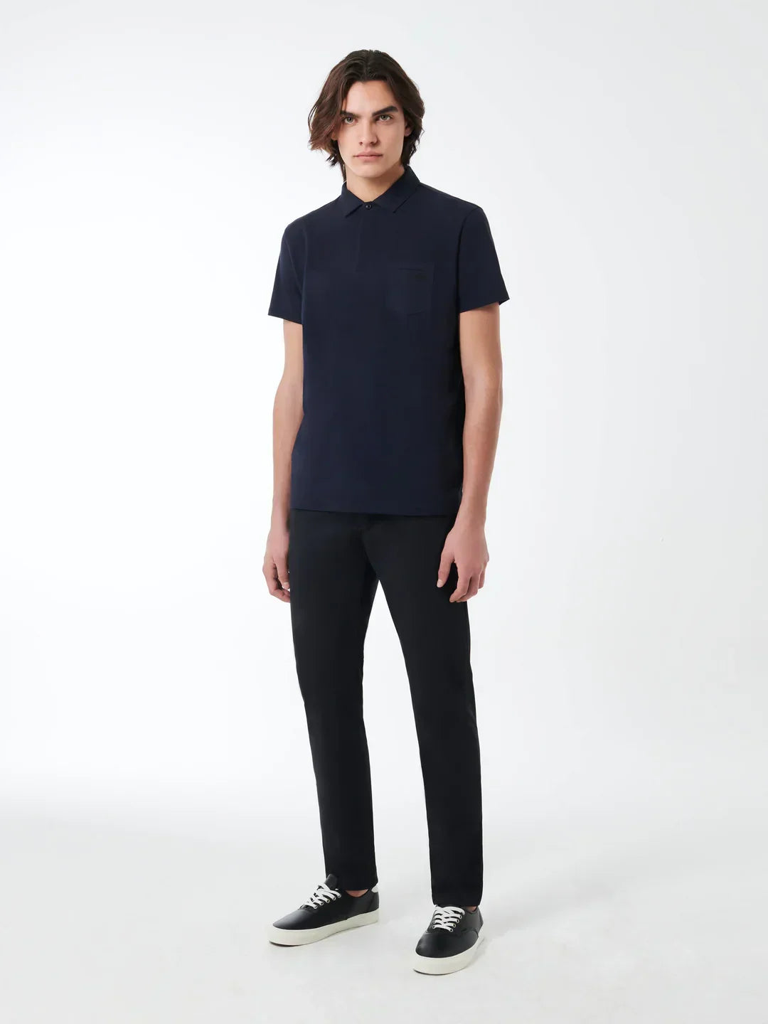 Modello uomo con polo blu scuro, pantaloni neri e sneakers, look casual elegante