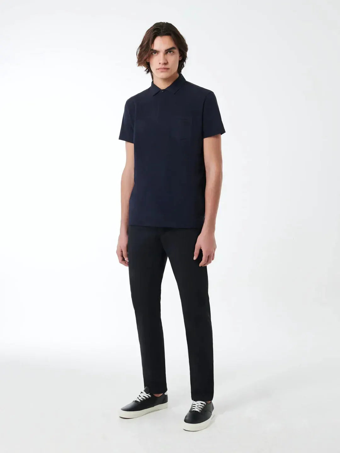 Modello uomo con polo blu scuro, pantaloni neri e sneakers, look casual elegante