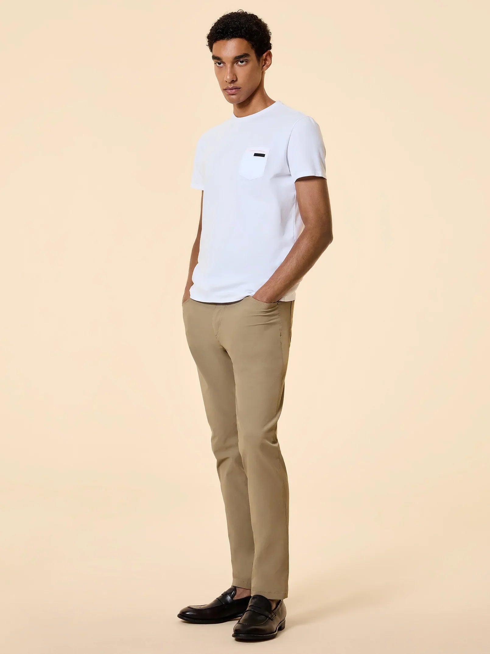 Modello uomo con t-shirt bianca, pantaloni beige e mocassini neri, stile elegante casual.