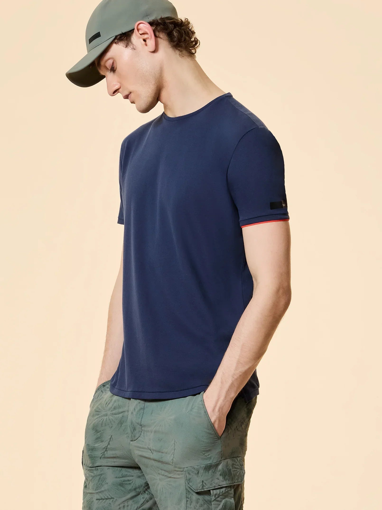 Modello indossa t-shirt blu, pantaloni cargo verdi e cappellino, moda uomo casual estiva.