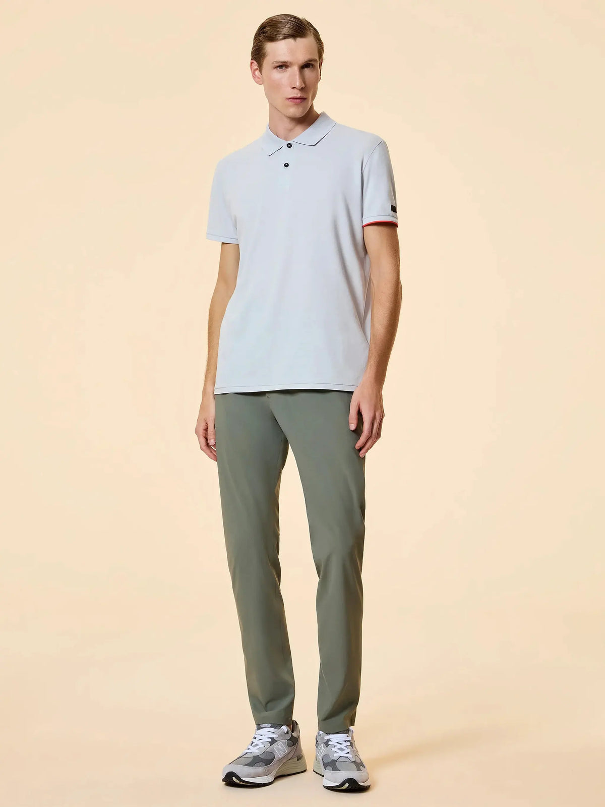 Modello uomo con polo chiara, pantaloni verdi e sneakers in look casual elegante