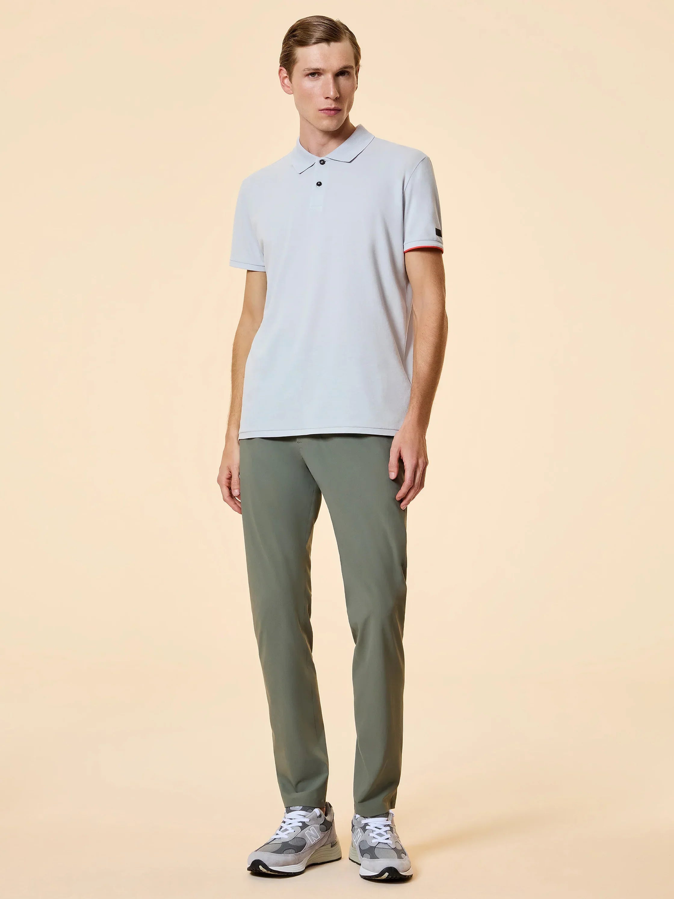 Modello uomo con polo chiara, pantaloni verdi e sneakers in look casual elegante