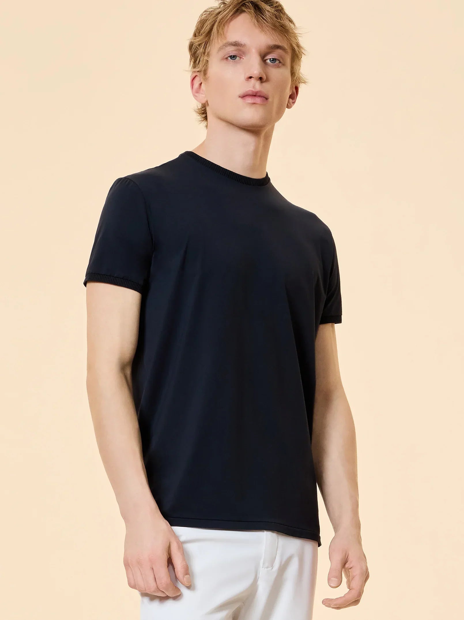 Modello uomo con t-shirt nera a maniche corte e pantaloni bianchi, sfondo neutro.