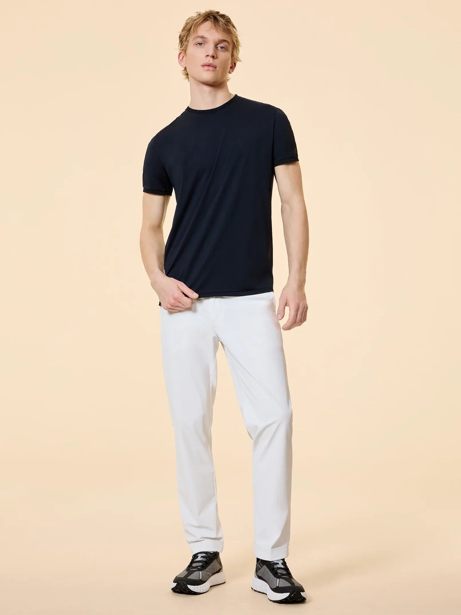 Modello uomo indossa t-shirt nera, pantaloni bianchi e sneakers nere, stile casual elegante.