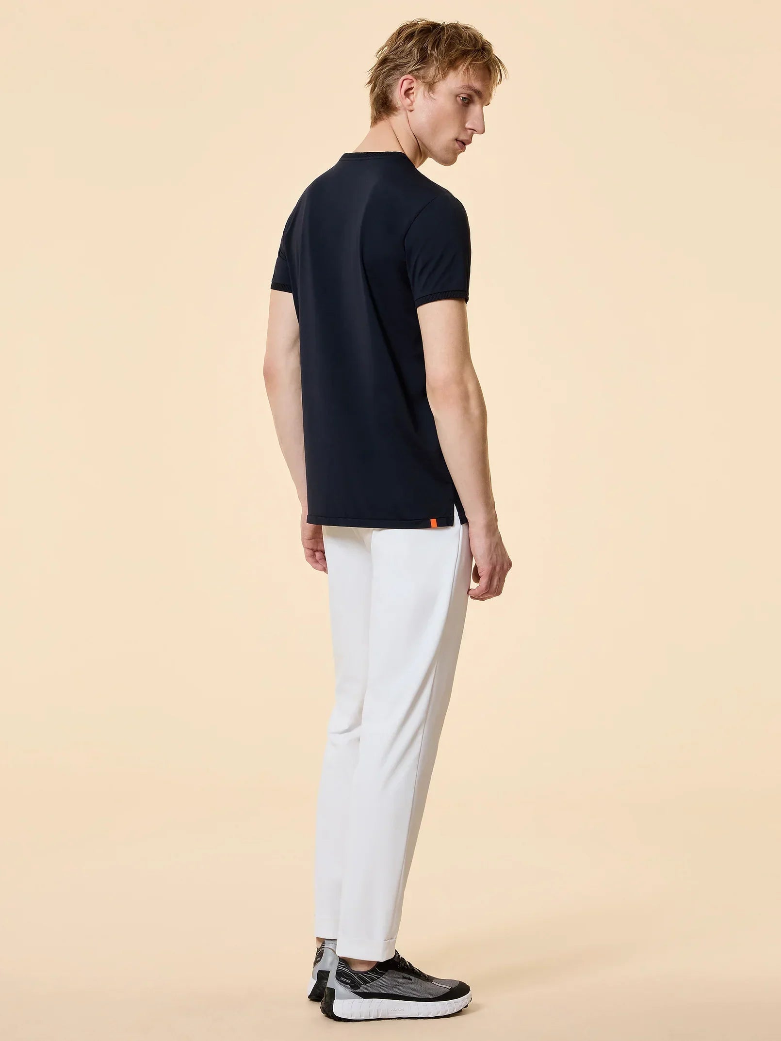 Modello uomo di profilo con t-shirt nera, pantaloni bianchi e sneakers nere, moda casual