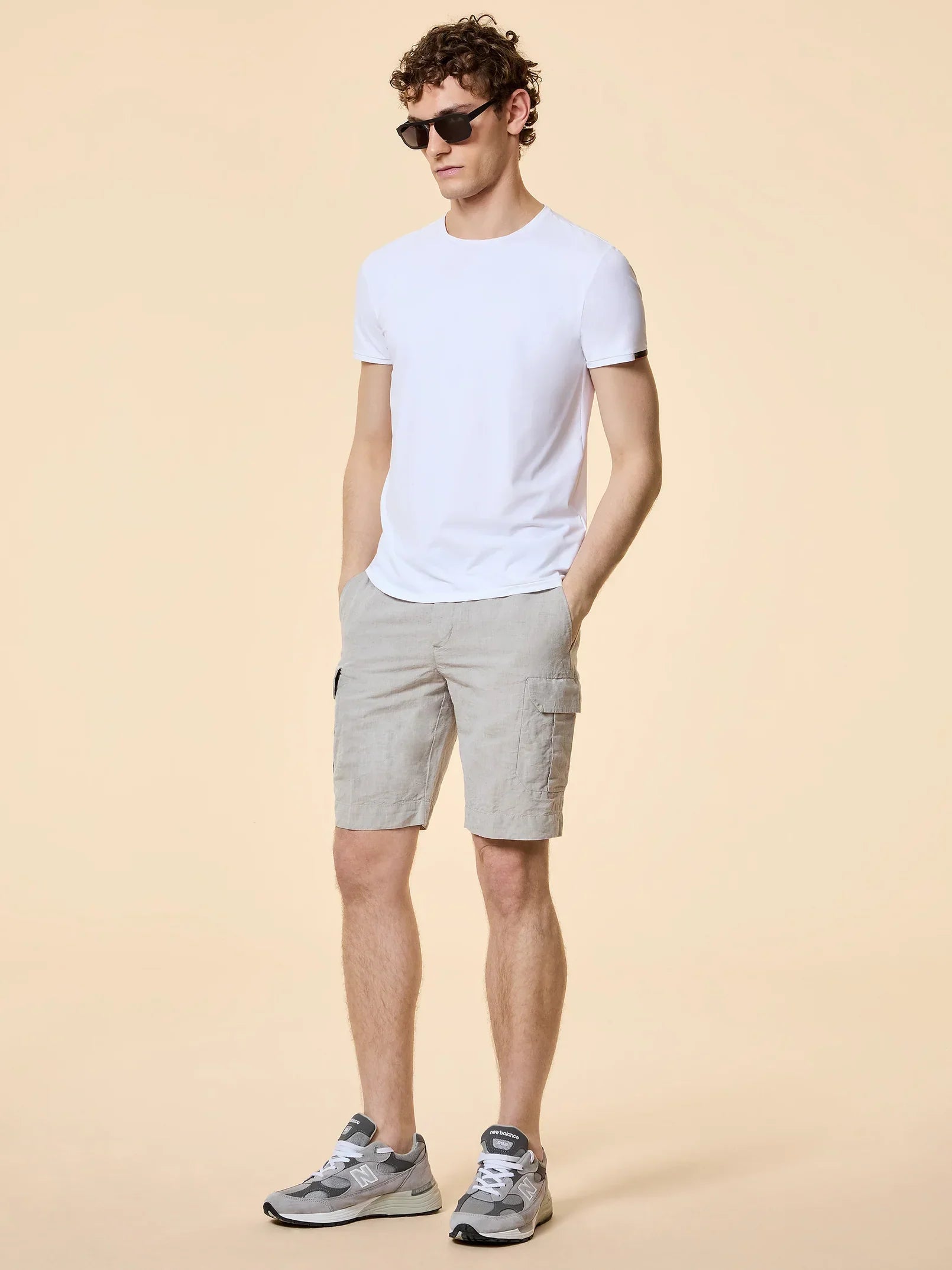 Uomo con t-shirt bianca, bermuda beige, sneakers grigie e occhiali da sole, moda casual estiva