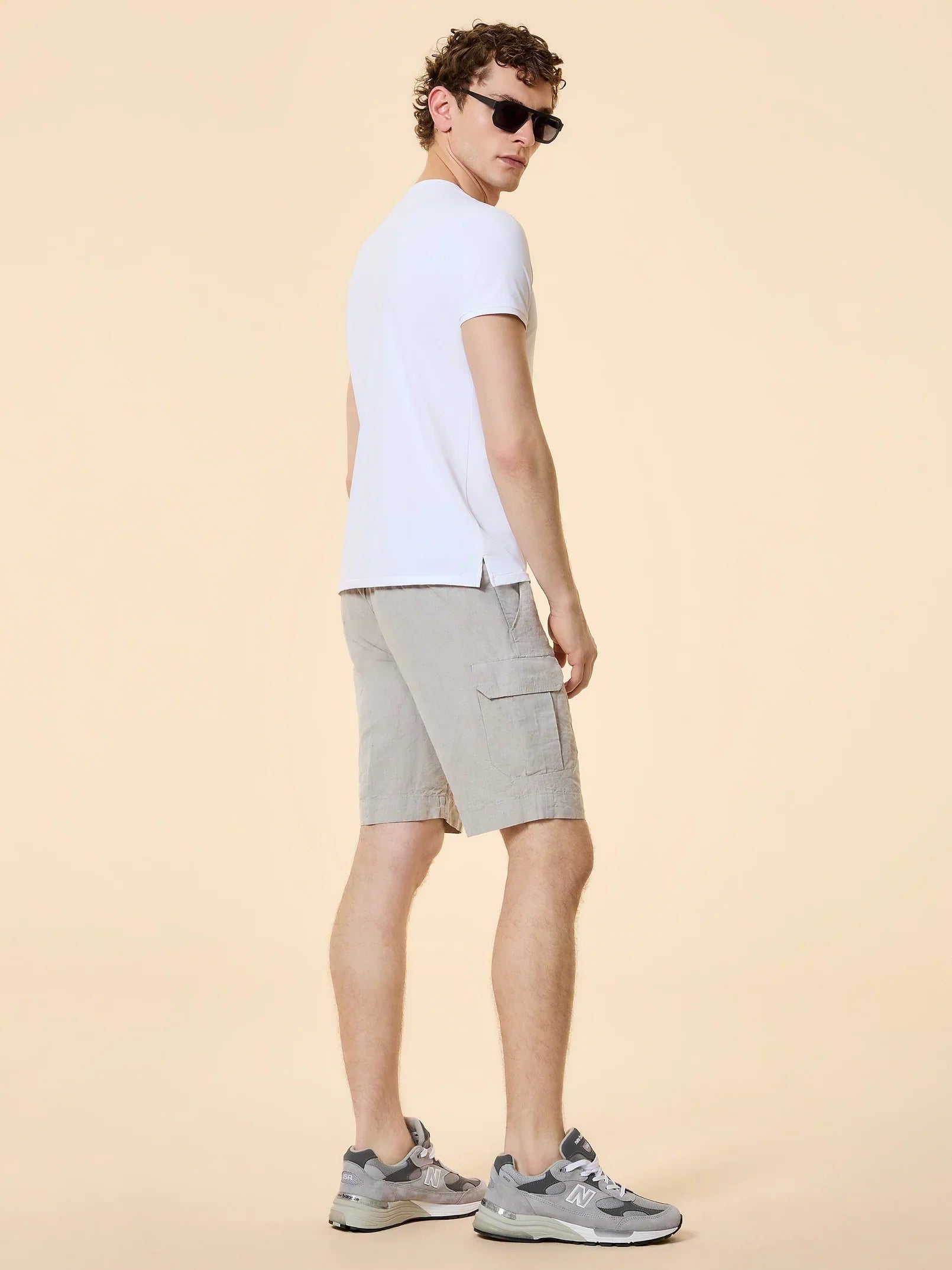 Uomo con t-shirt bianca, bermuda beige e sneakers grigie, look casual estivo