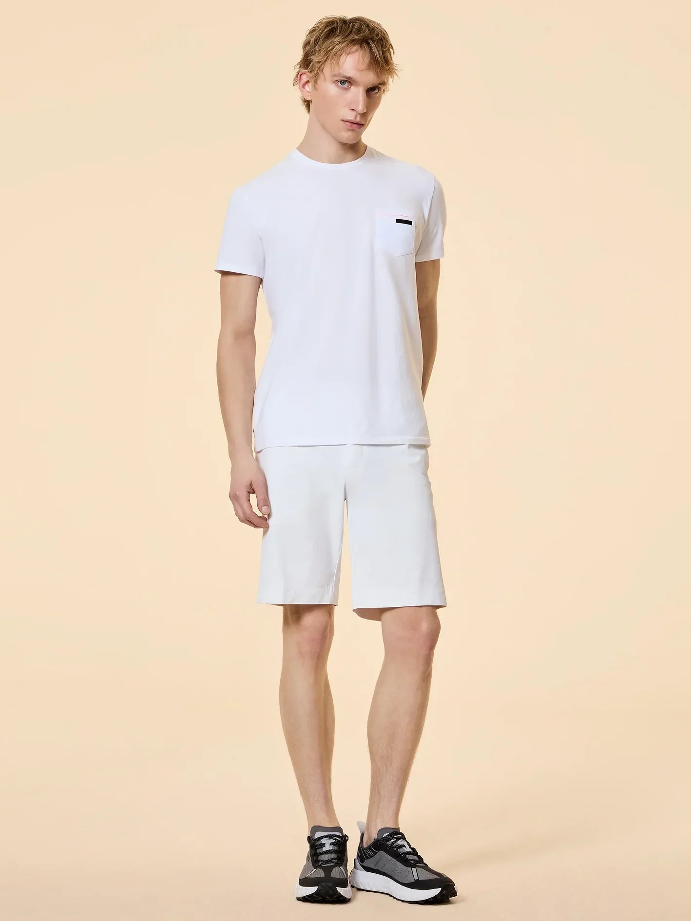 Modello uomo con t-shirt bianca, bermuda bianchi e sneakers nere, abbigliamento estivo casual.