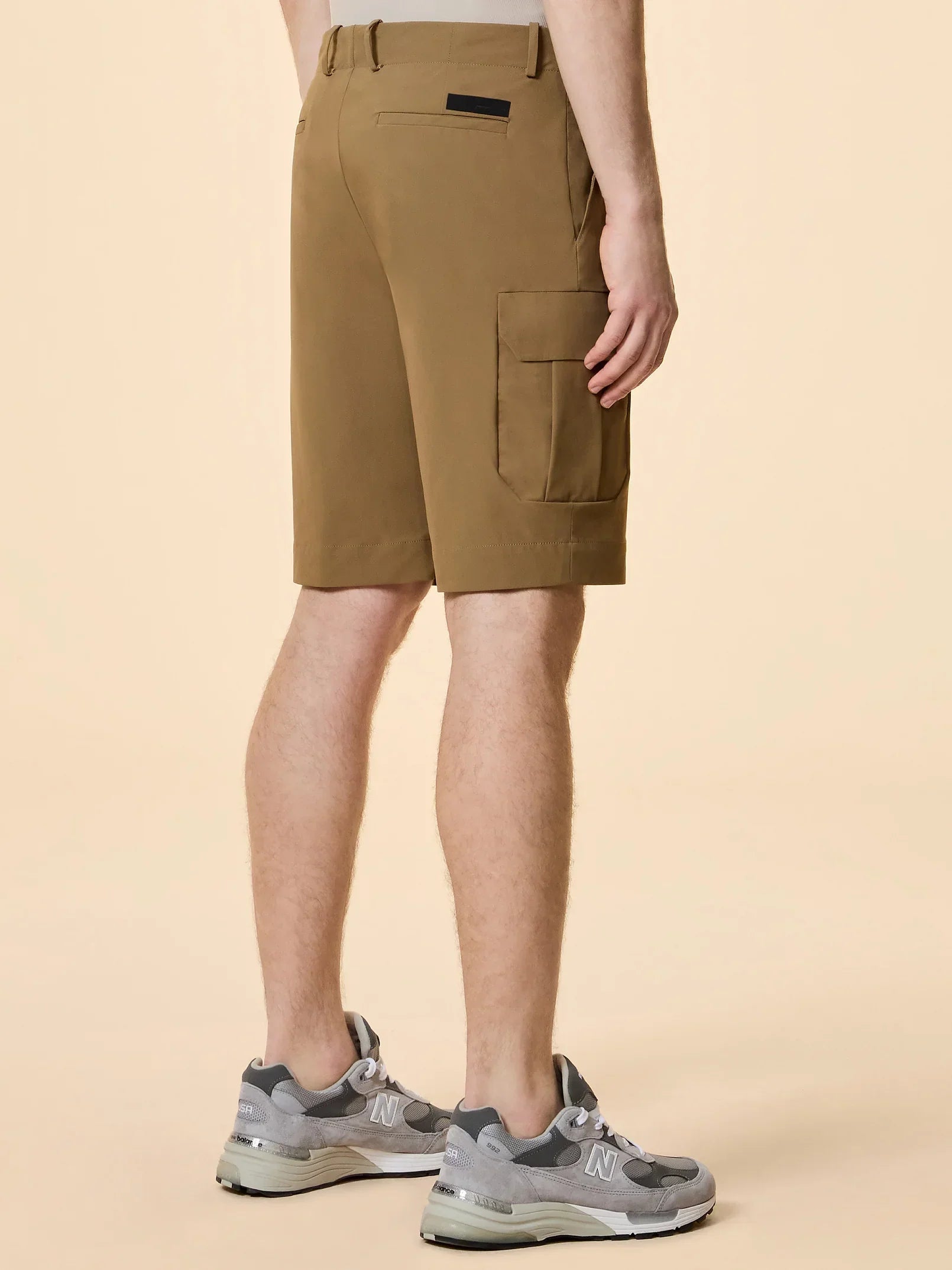 Shorts cargo uomo color cammello con tasche laterali, scarpe sportive grigie, stile casual.