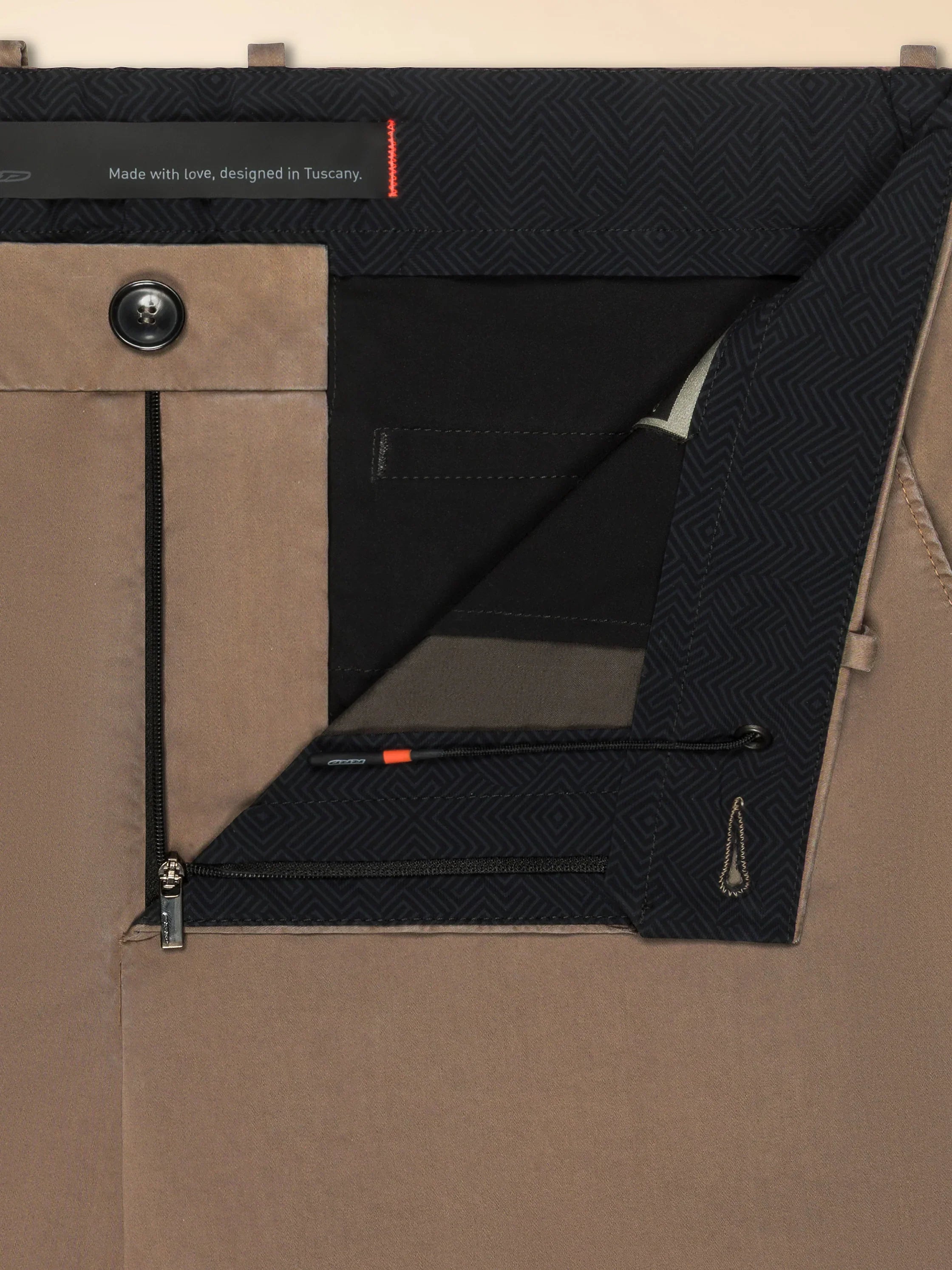 Dettaglio pantalone uomo beige con interno fantasia geometrica, chiusura zip e bottone.