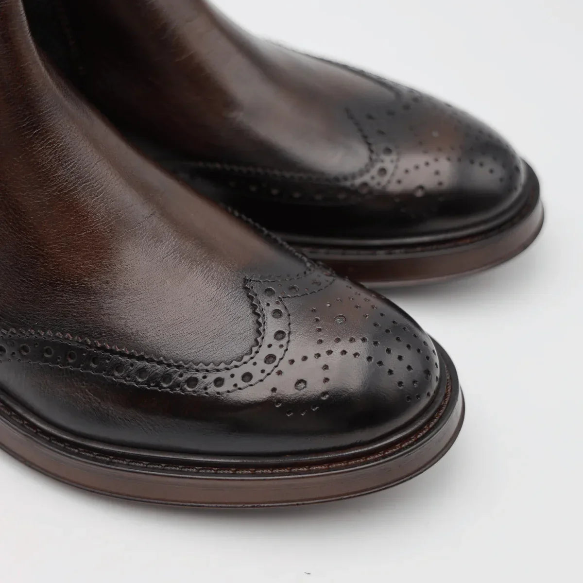 Dettaglio scarpe uomo in pelle marrone con motivo brogue su punta, eleganti e raffinate.
