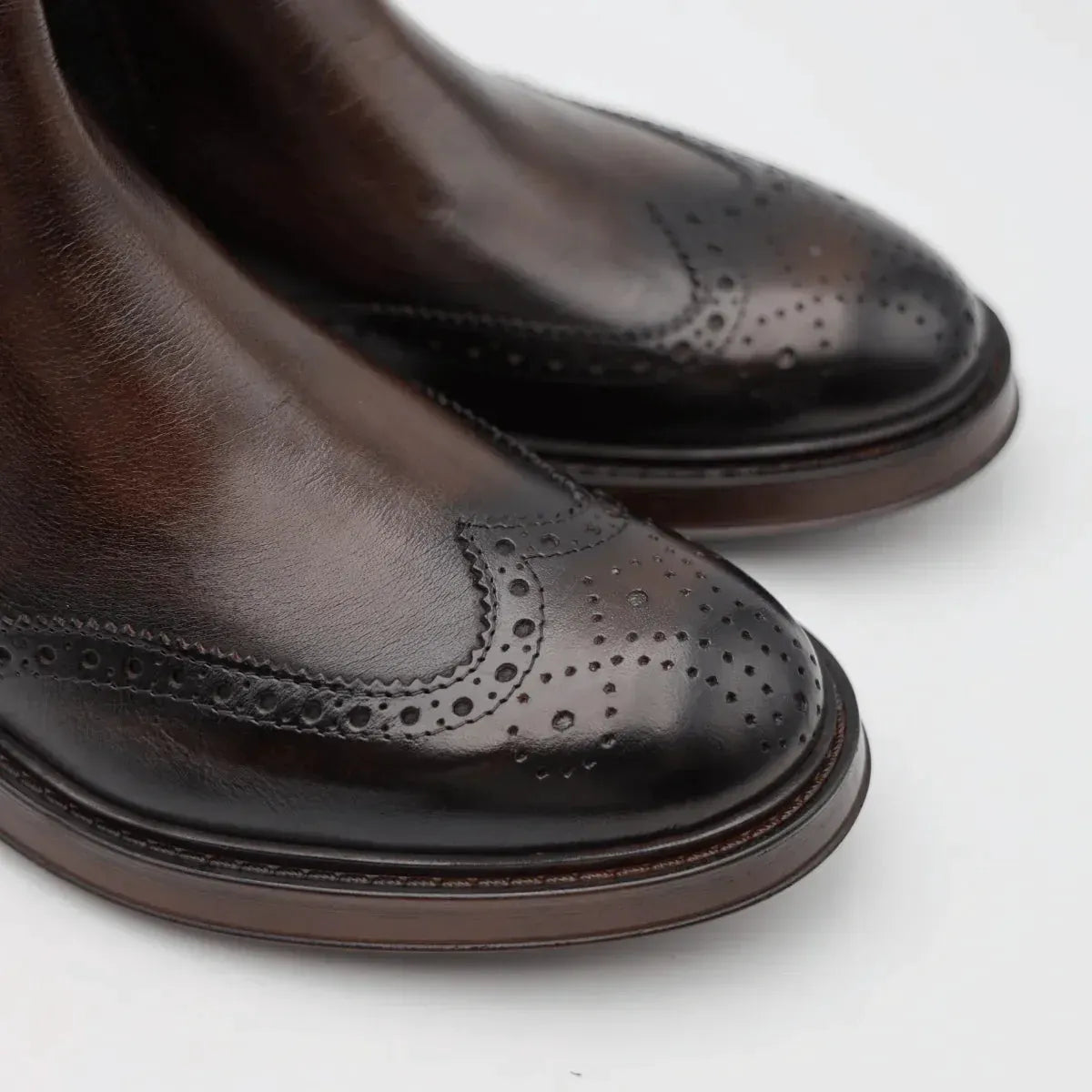Dettaglio scarpe uomo in pelle marrone con motivo brogue su punta, eleganti e raffinate.