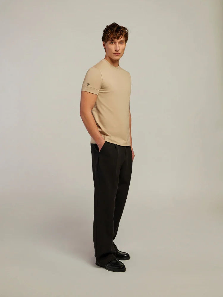 Uomo indossa t-shirt beige e pantaloni neri eleganti, moda uomo minimal su sfondo neutro.