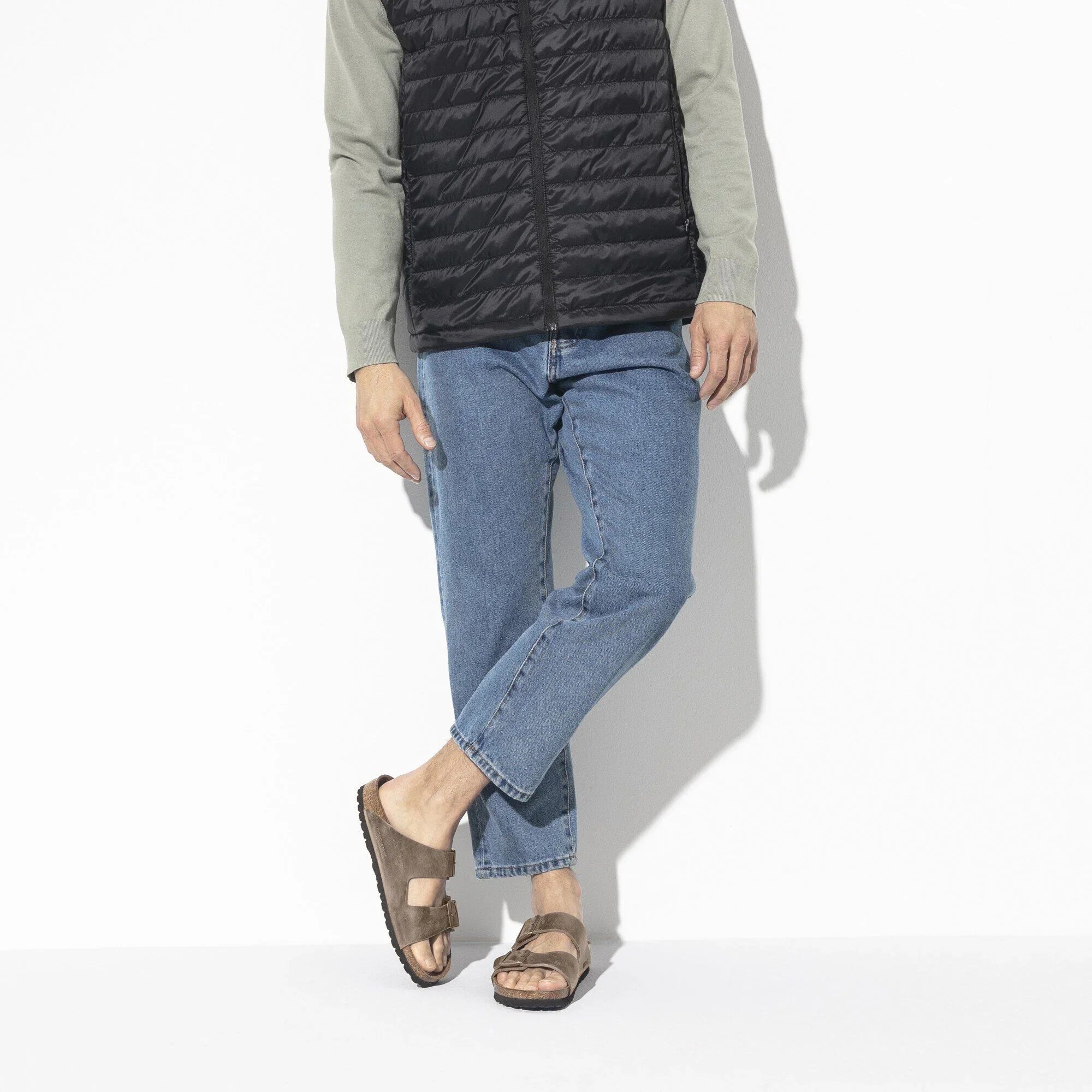 Look uomo casual con gilet nero, jeans azzurri e sandali marroni da uomo
