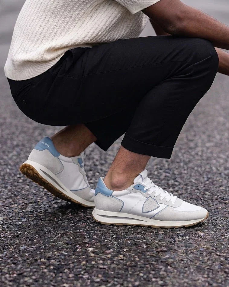 Sneakers uomo bianche e azzurre moda casual su asfalto, pantaloni neri, stile elegante.
