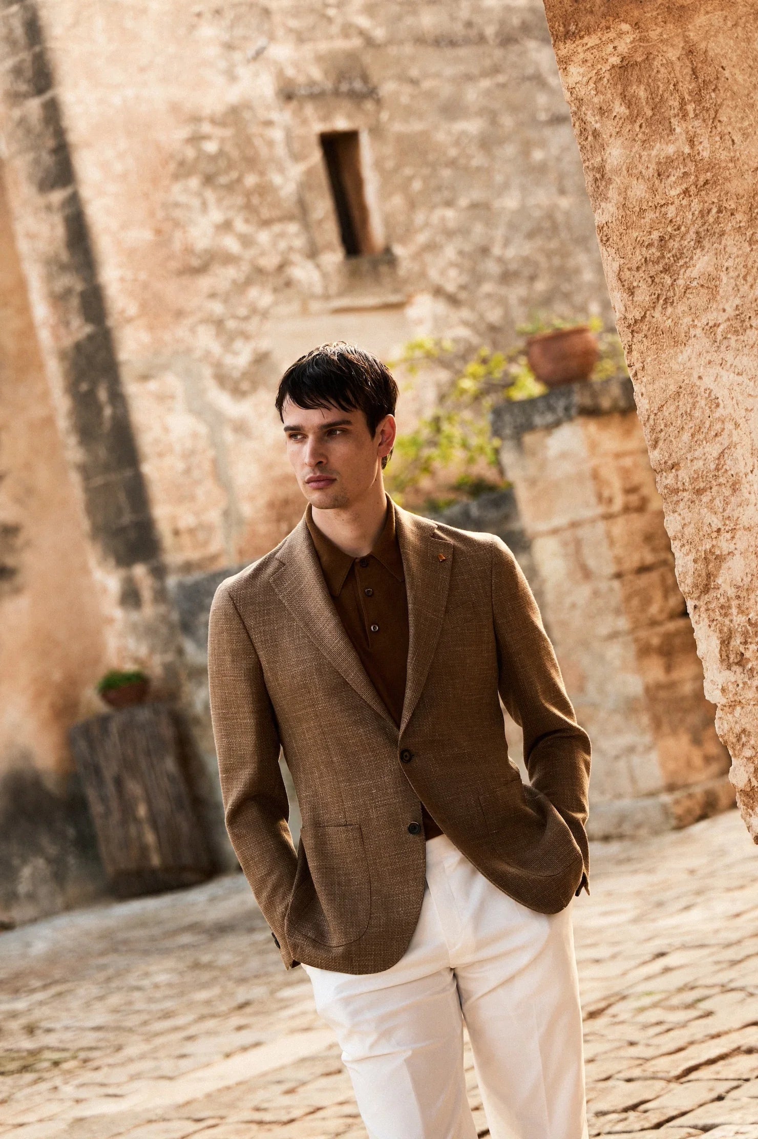 Uomo con giacca elegante marrone e pantaloni bianchi, moda abbigliamento uomo, fondo rustico.
