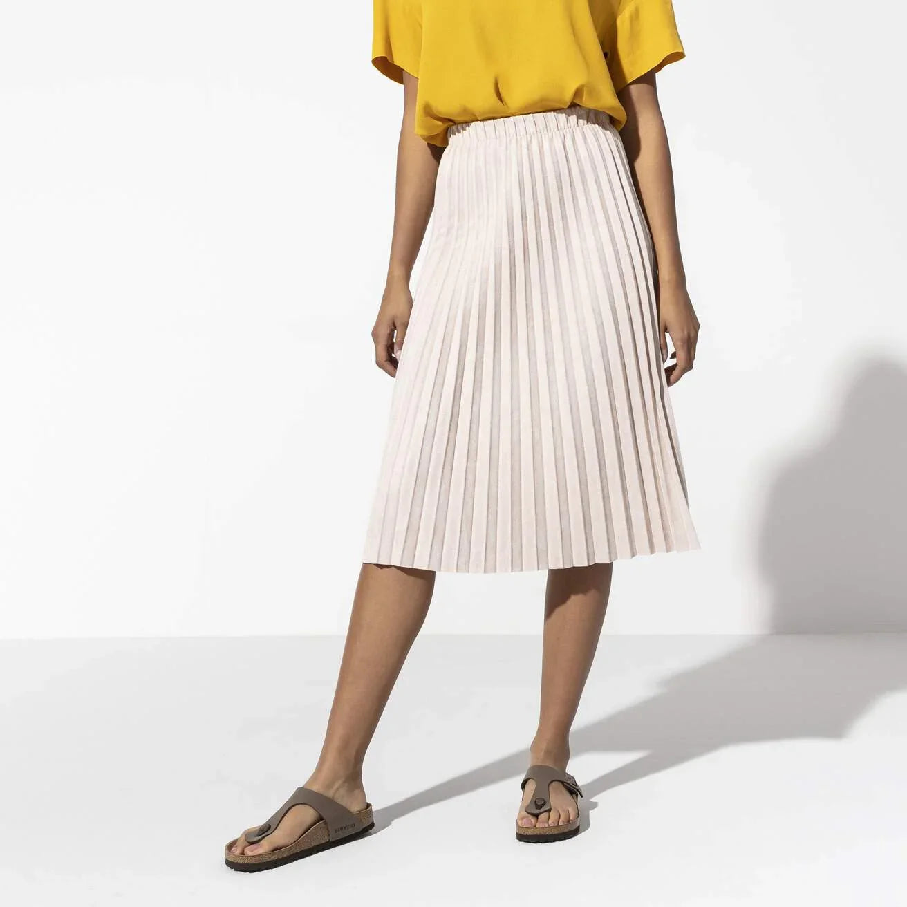 Gonna plissettata beige da donna, abb abbigliamento estivo, con sandali e maglia gialla.