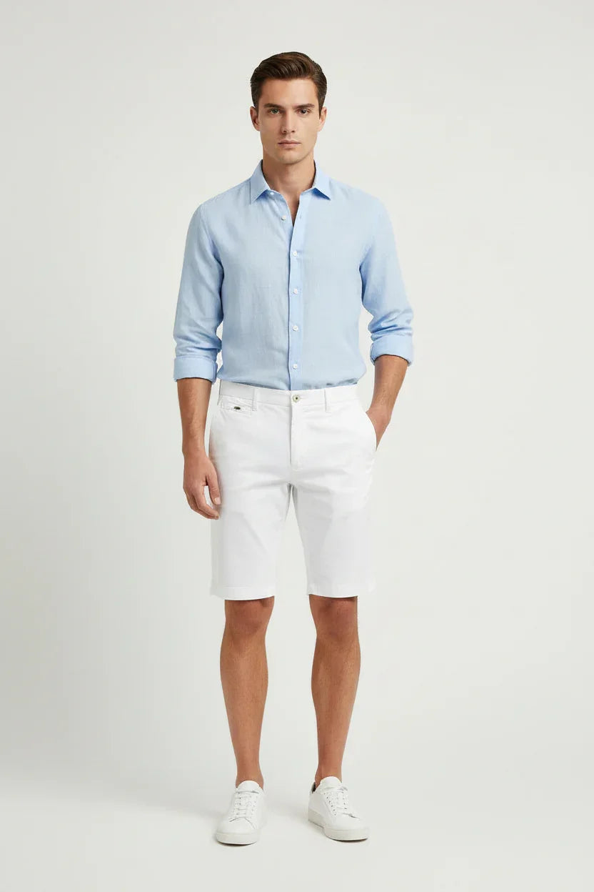 Modello indossa camicia azzurra e bermuda bianchi uomo, look estivo elegante.