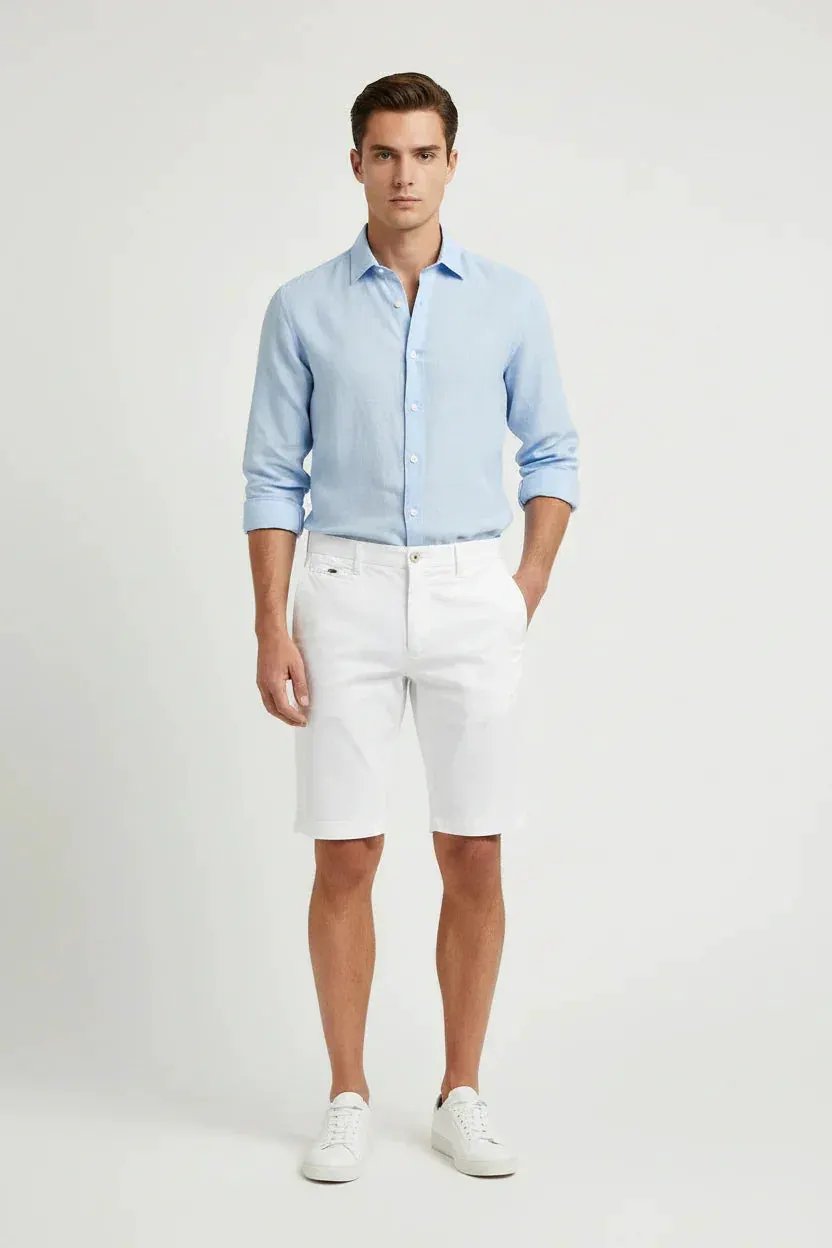 Modello indossa camicia azzurra e bermuda bianchi uomo, look estivo elegante.