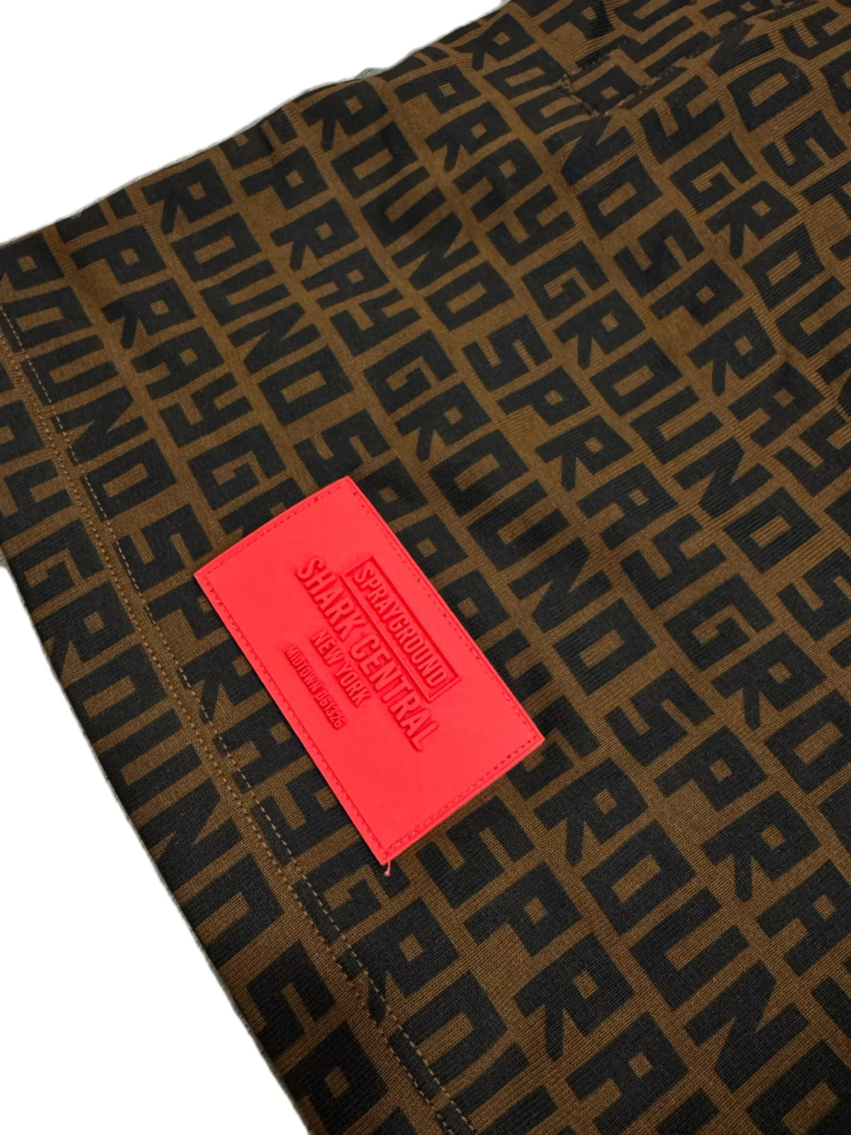 Dettaglio pantalone marrone con stampa logata nera e patch rossa Sprayground in rilievo.