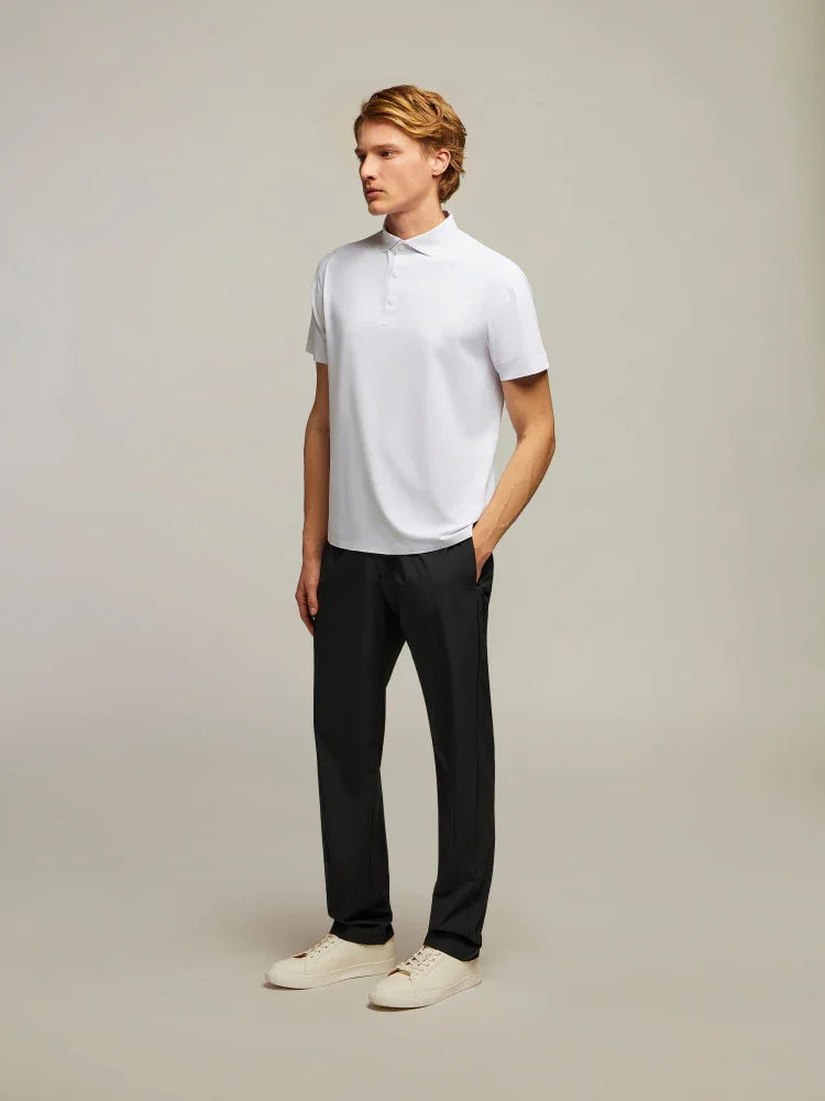 Modello uomo con polo bianca a maniche corte, pantaloni neri e sneakers beige su sfondo neutro