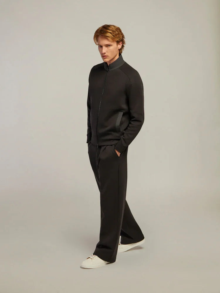 Modello uomo indossa tuta nera elegante con giacca zip, pantaloni ampi e sneakers bianche
