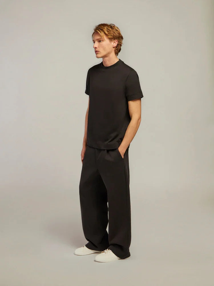 Modello uomo indossa t-shirt e pantaloni neri larghi, look minimal elegante, scarpe bianche.