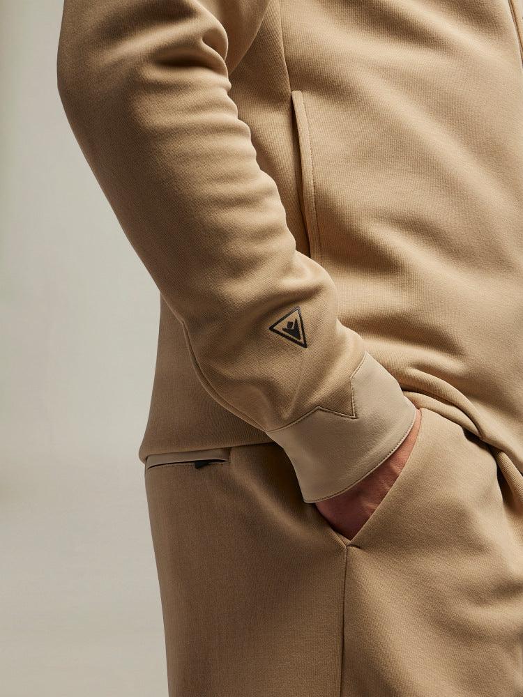 Dettaglio di tuta beige uomo, felpa con logo sulla manica e tasca laterale.