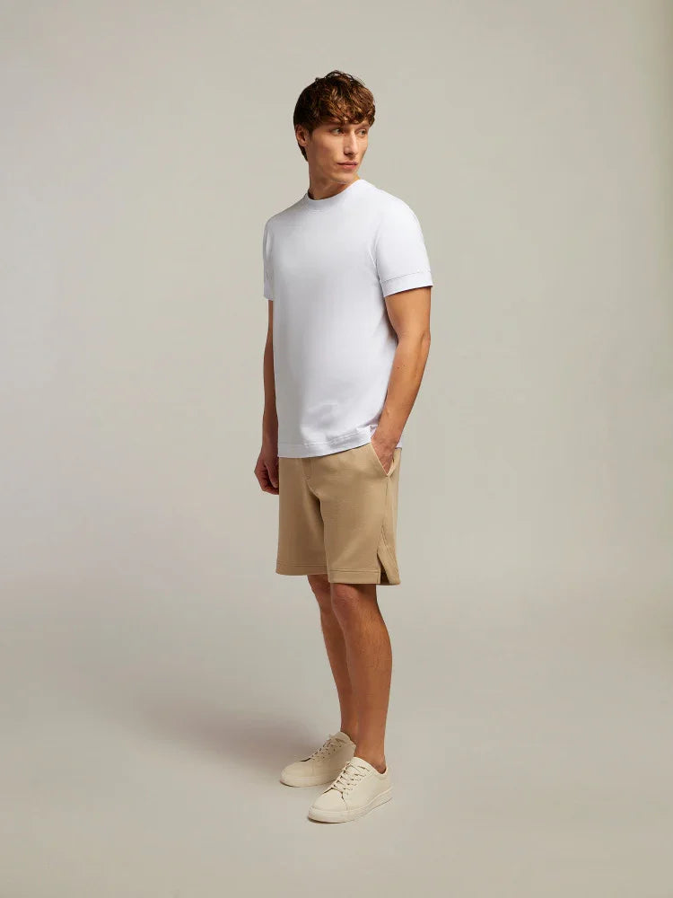 Modello uomo con t-shirt bianca, bermuda beige e sneakers, look casual estivo elegante.