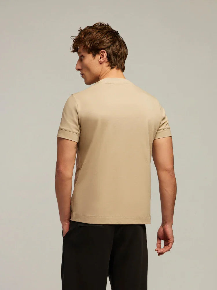 Uomo indossa t-shirt beige a maniche corte e pantaloni neri, visto di schiena, su sfondo neutro.