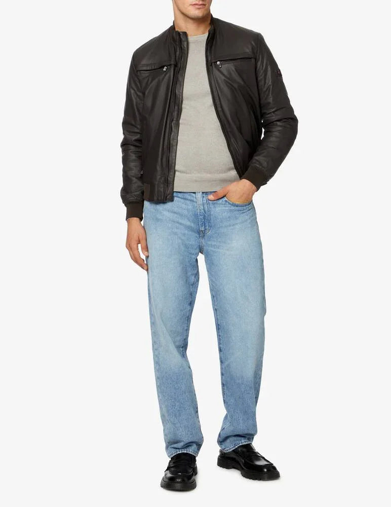 Modello uomo con giacca in pelle nera, maglia grigia, jeans chiari e mocassini neri.