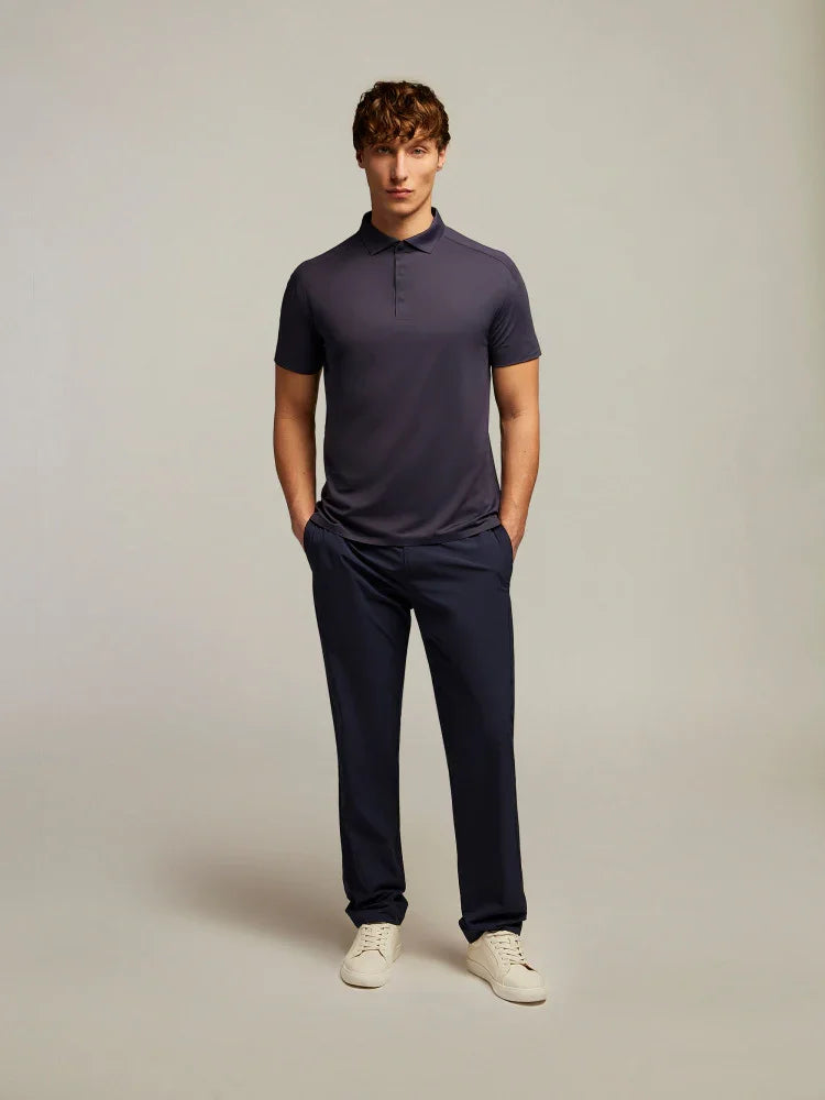 Modello uomo indossa polo blu scuro, pantaloni eleganti navy e sneakers bianche su sfondo neutro.