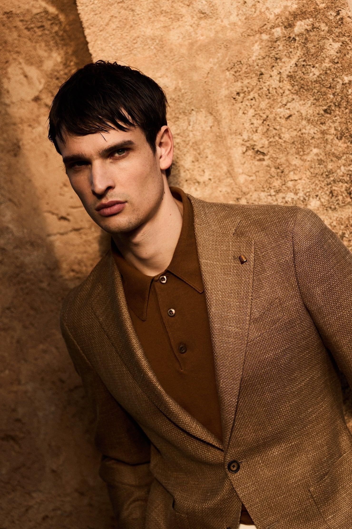 Modello uomo con giacca elegante marrone e polo coordinata su sfondo beige, moda uomo