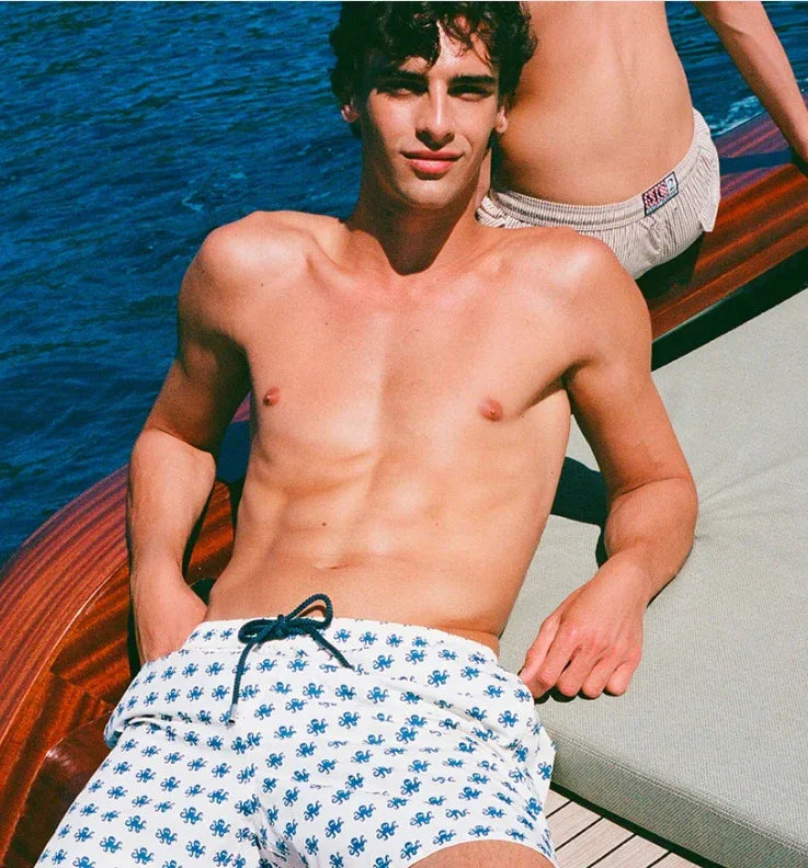 Uomo in costume da bagno bianco con stampa blu su barca, moda mare uomo estate.
