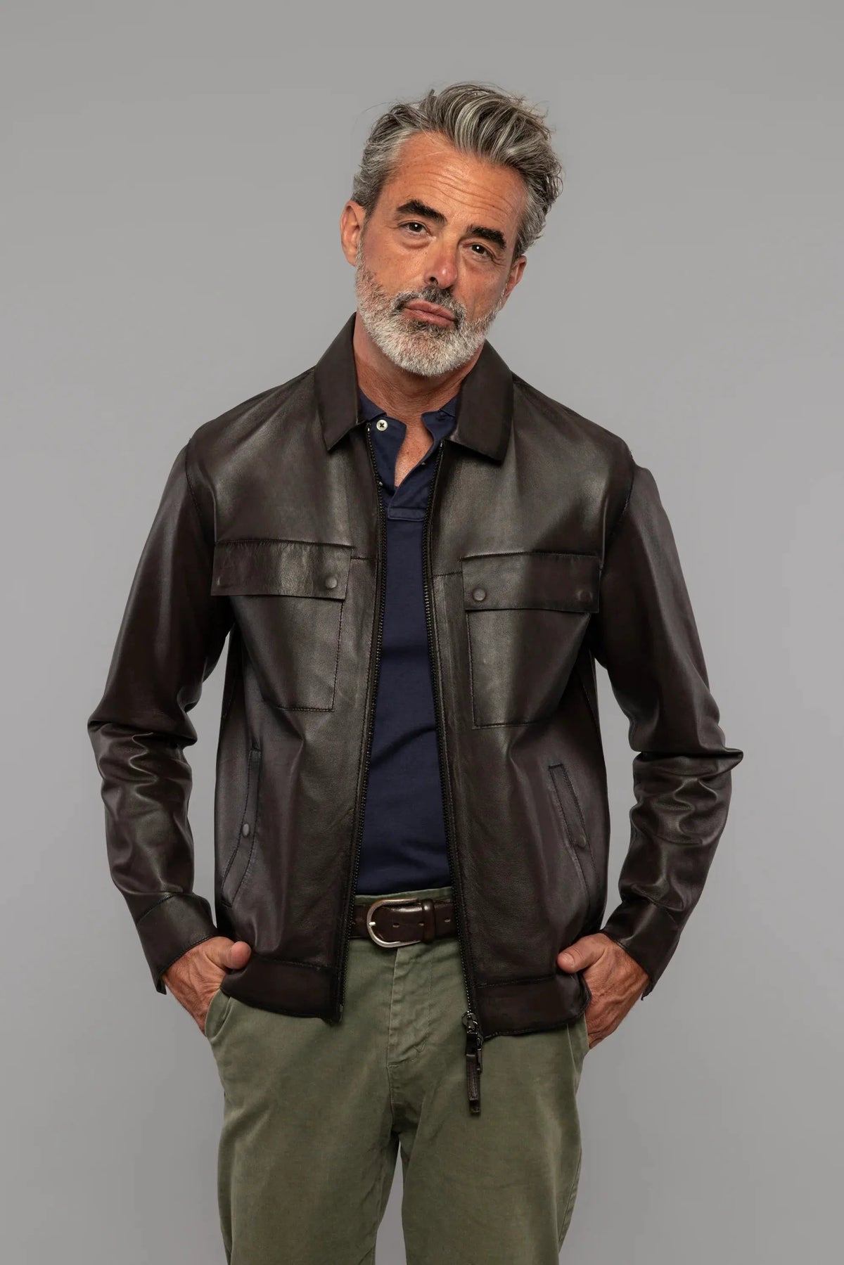 Giacca uomo in pelle marrone, camicia blu, pantaloni verdi, stile casual elegante.