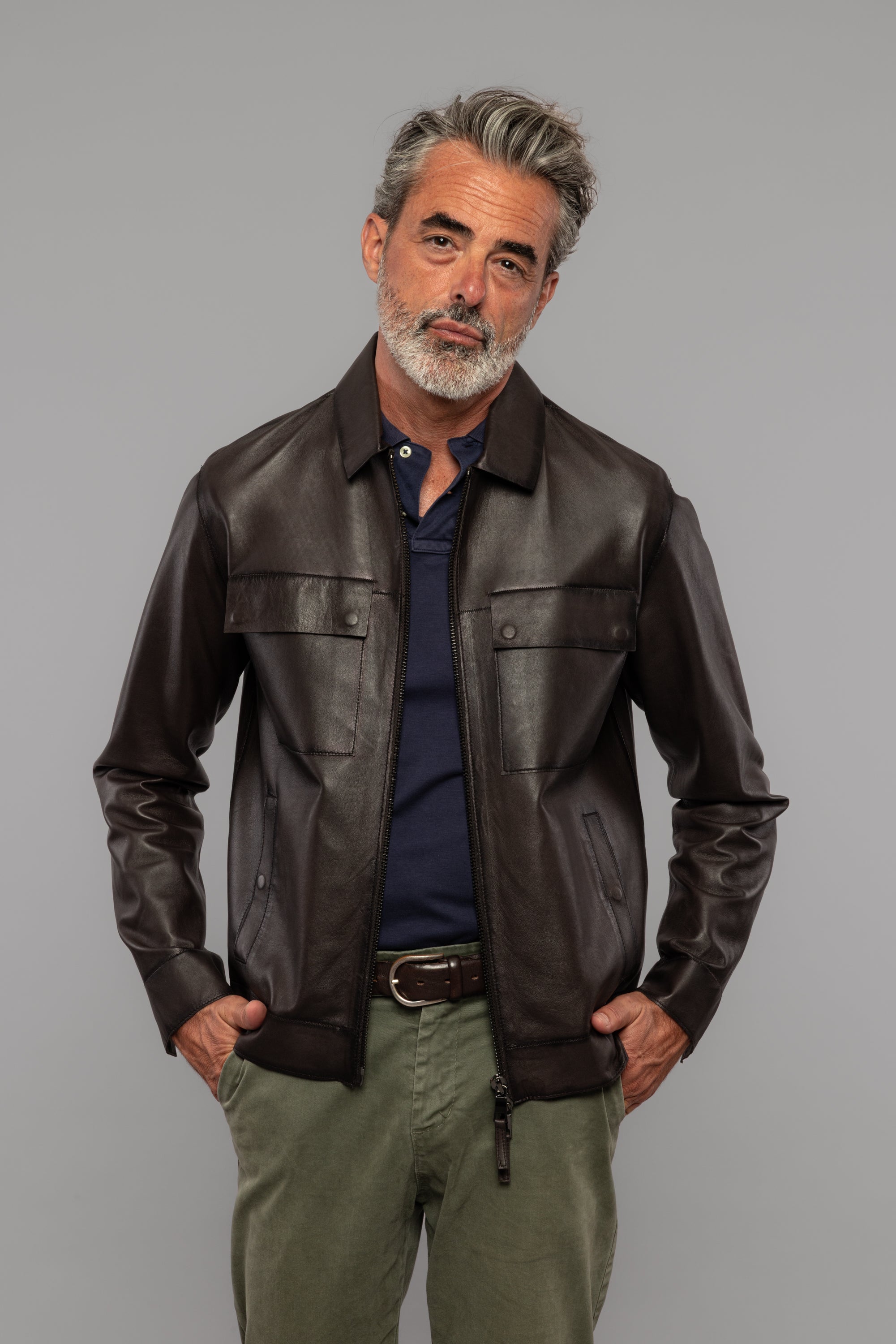 Giacca uomo in pelle marrone, camicia blu, pantaloni verdi, stile casual elegante.