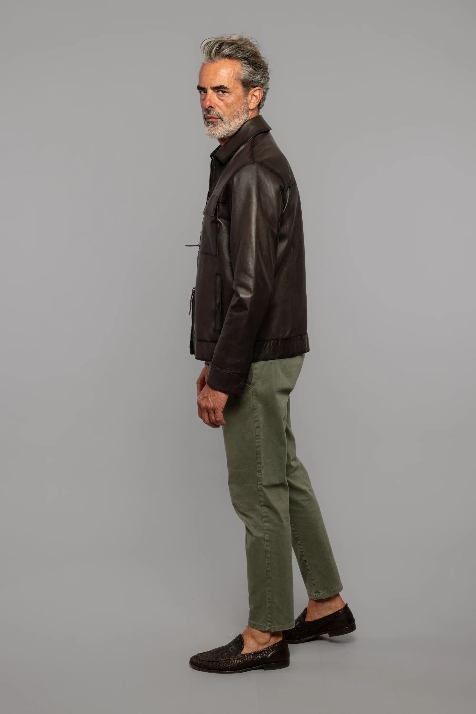 Uomo maturo con giacca in pelle marrone, pantaloni verde oliva e mocassini scuri