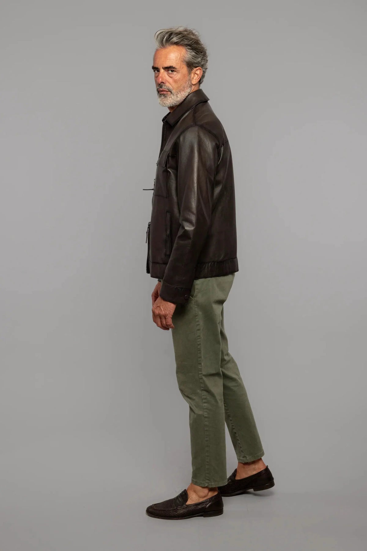 Uomo maturo con giacca in pelle marrone, pantaloni verde oliva e mocassini scuri