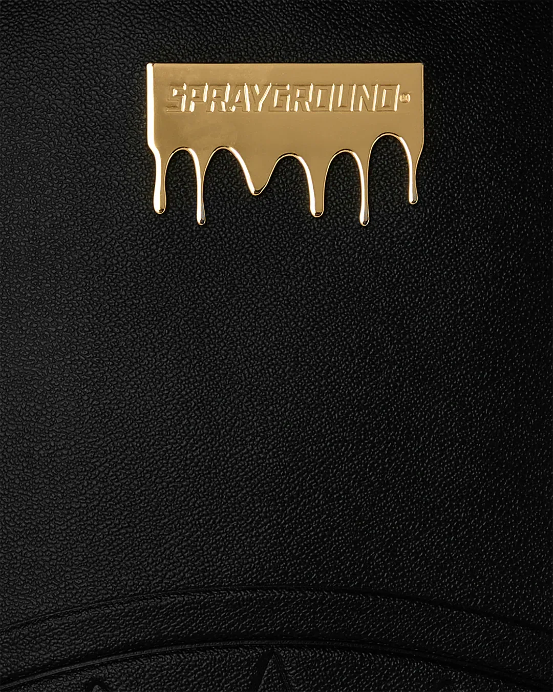 Dettaglio di logo dorato Sprayground su sfondo in pelle nera, accessorio moda elegante.