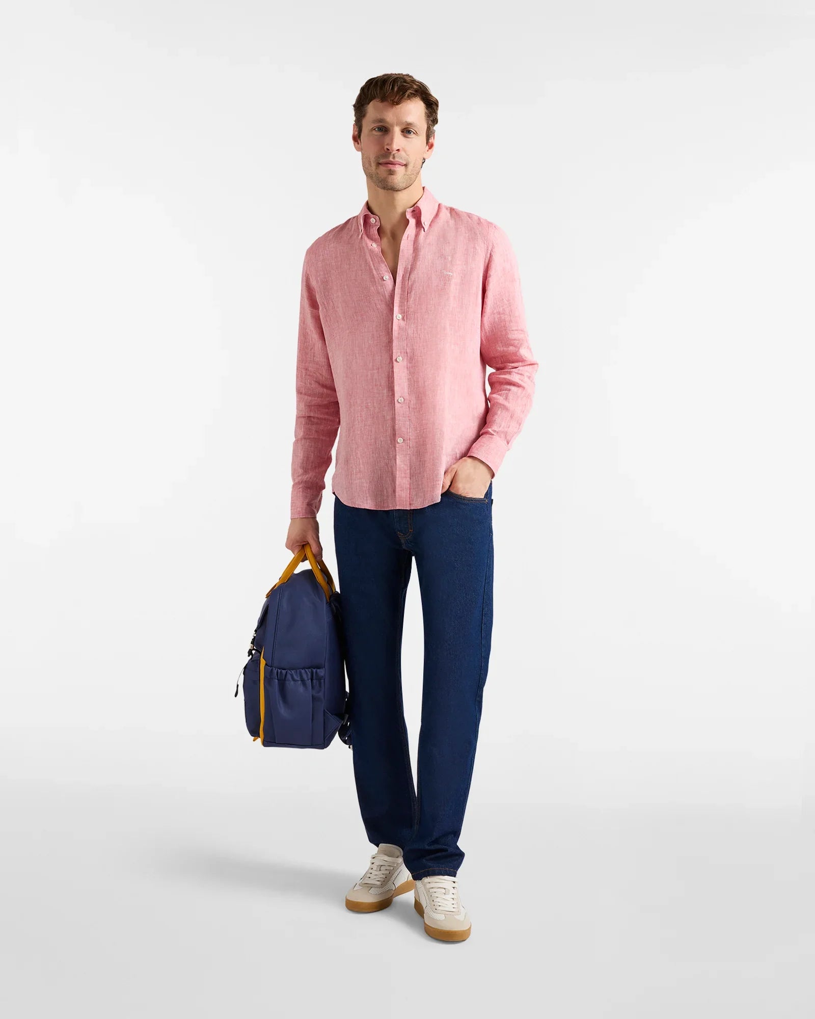 Uomo con camicia rosa in lino, jeans blu, sneaker bianche e zaino blu, moda casual uomo