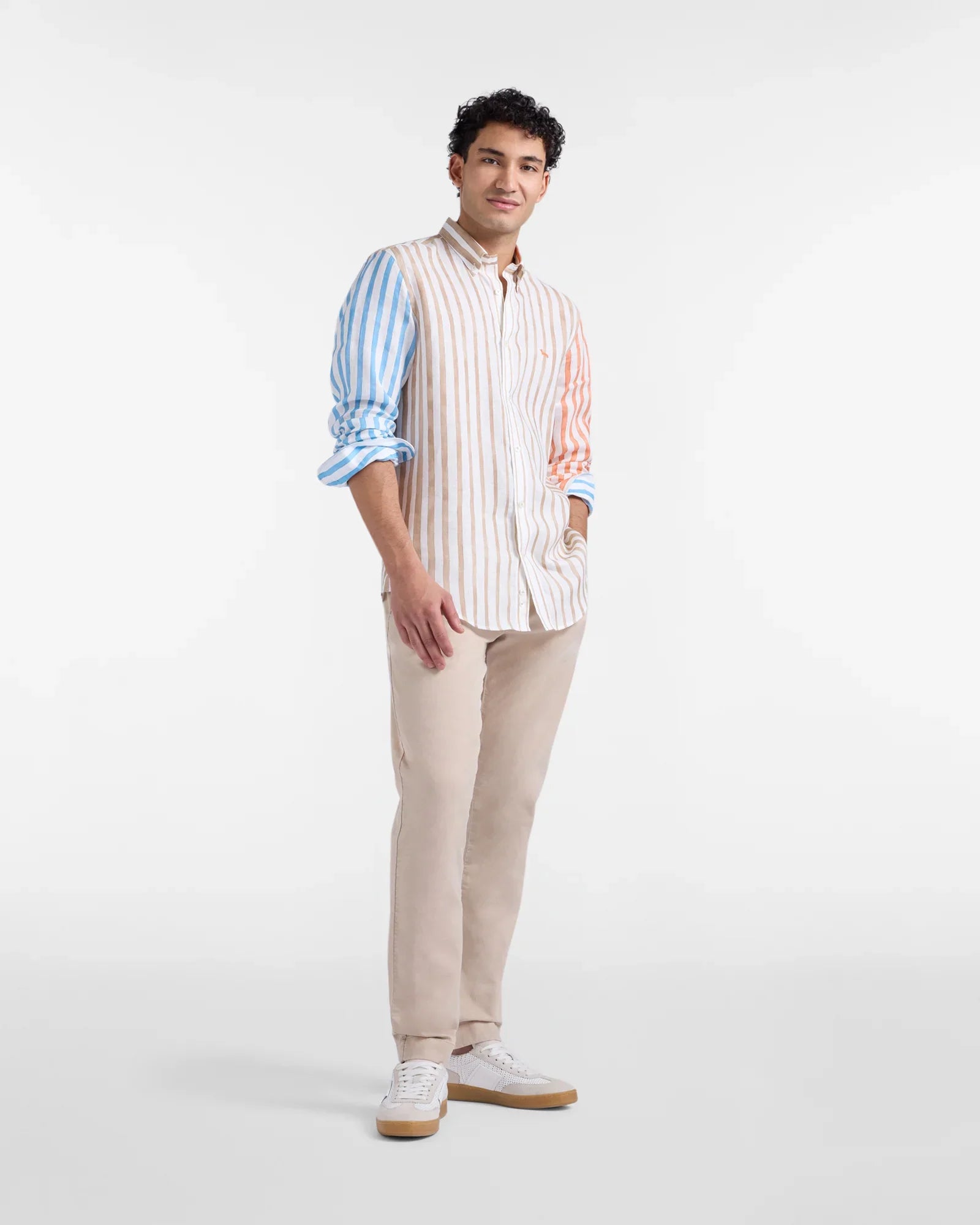 Modello indossa camicia a righe multicolore e pantaloni beige, stile moda uomo elegante casual.