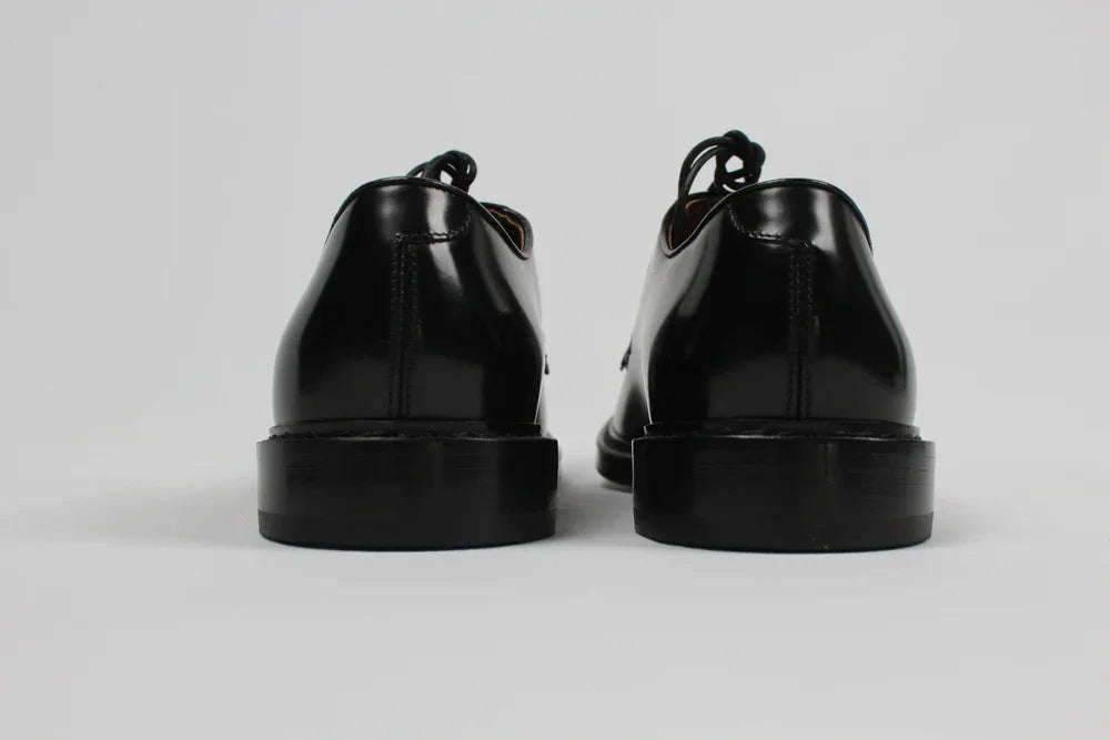 Scarpe derby uomo nere in pelle lucida viste da dietro su sfondo neutro