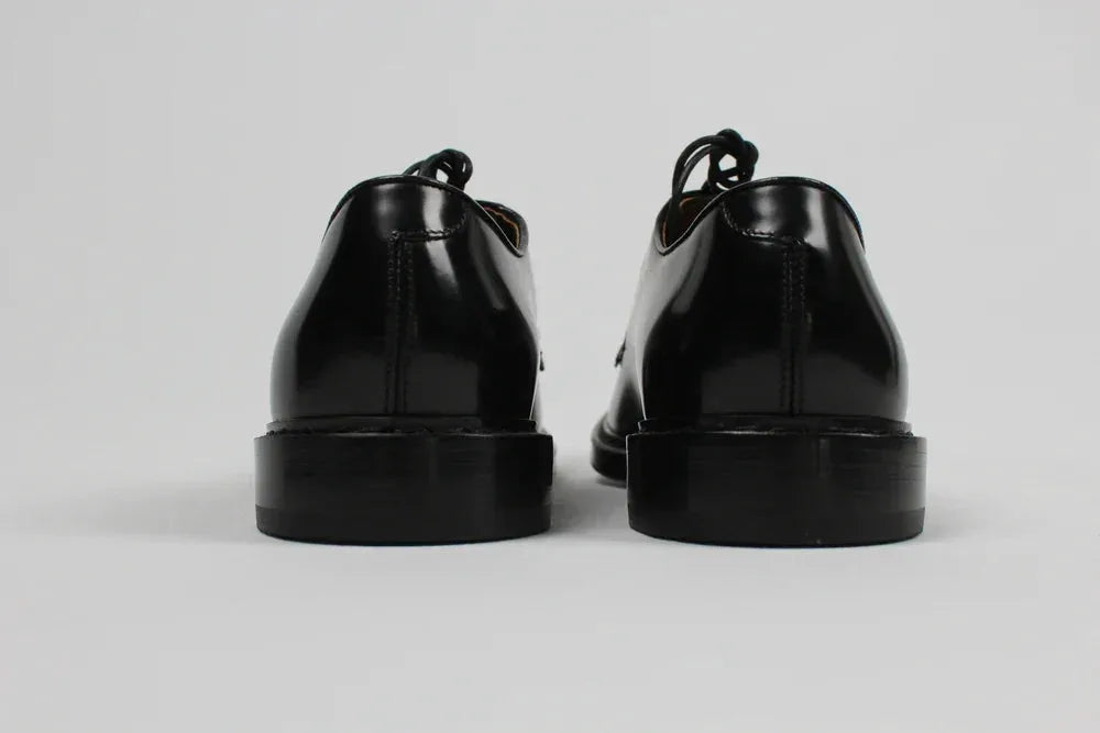 Scarpe derby uomo nere in pelle lucida viste da dietro su sfondo neutro