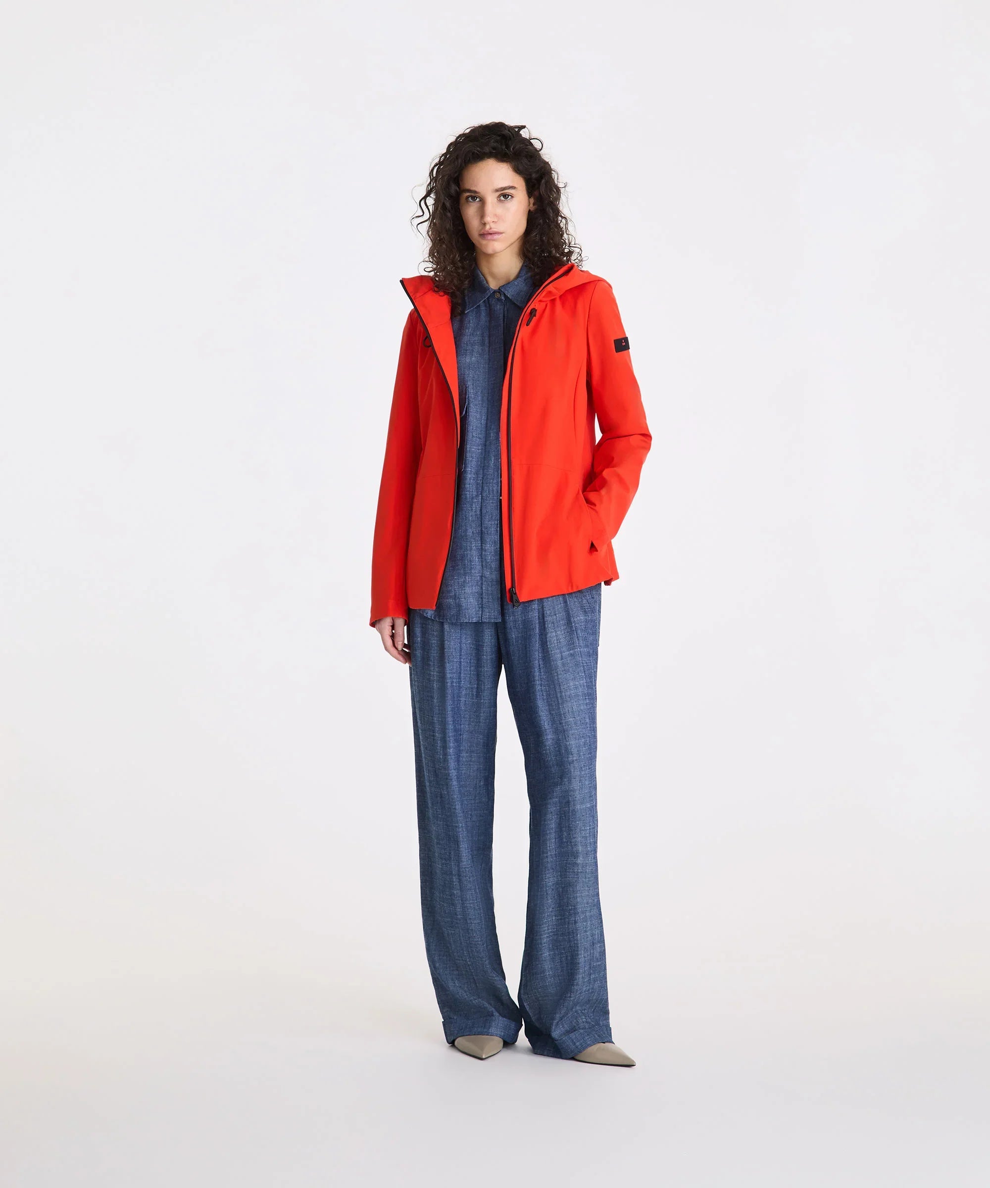 Donna con giacca arancione, pantaloni blu ampi e scarpe beige, stile casual elegante.