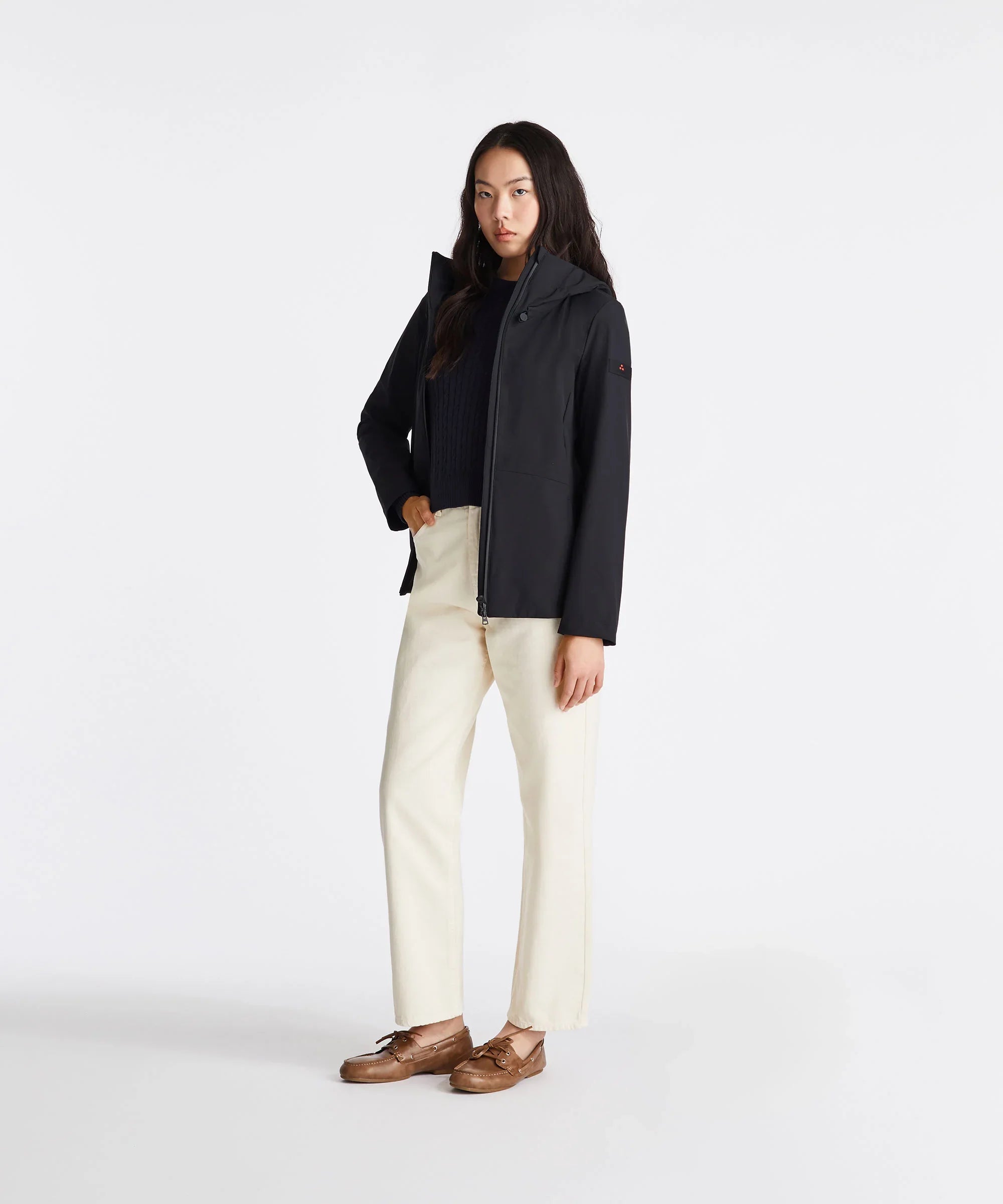 Donna con giacca nera impermeabile, maglione blu, pantaloni chiari e mocassini marroni